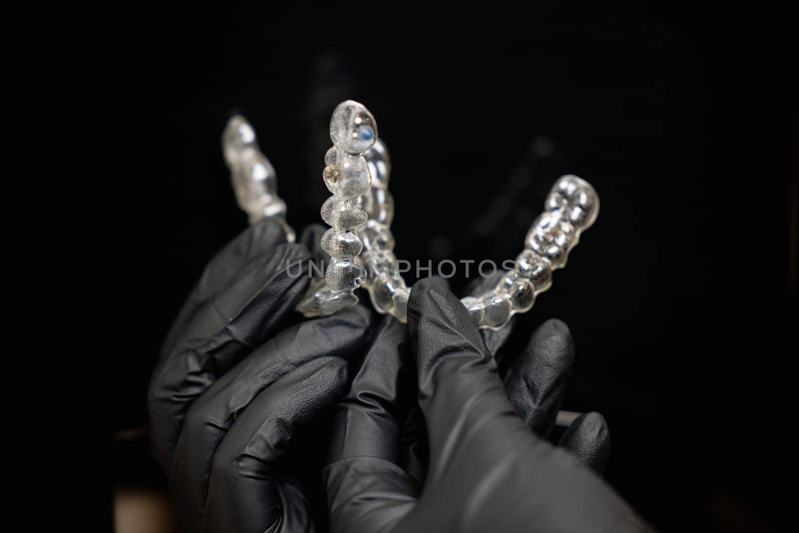 doctors hands in black gloves holding silicone mouth guard by yulikov