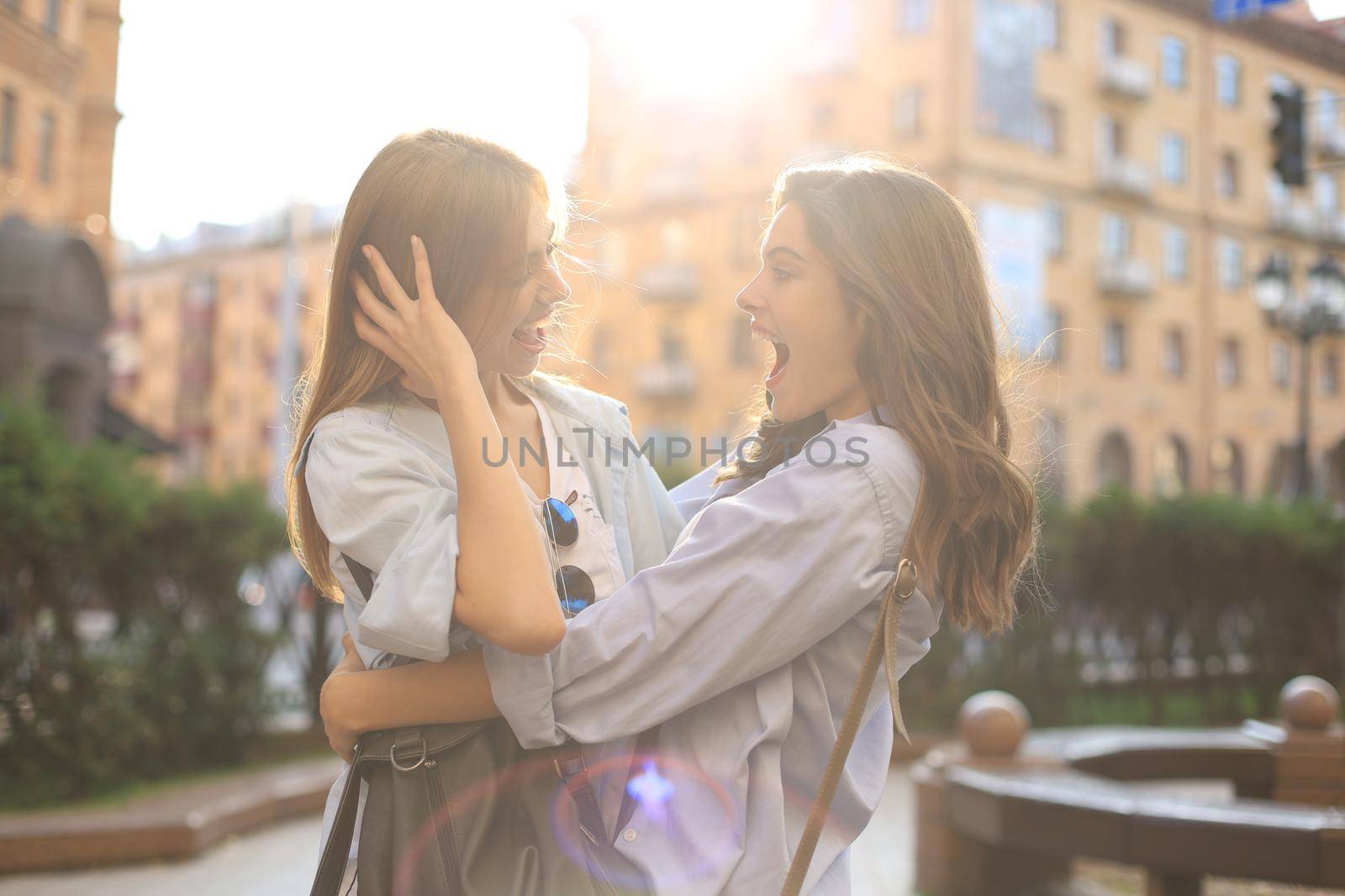 Two young smiling hipster women in summer clothes posing on street.Female showing positive face emotions