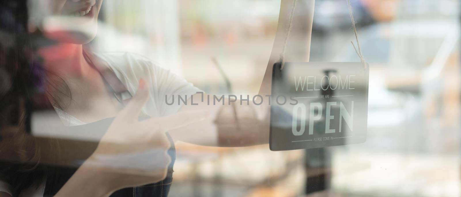 Portrait of smiling young barista girl in apron holding open sign board while standing at her cafe. elegant asian coffee shop female staff turn door plate in the morning in own store small business by nateemee