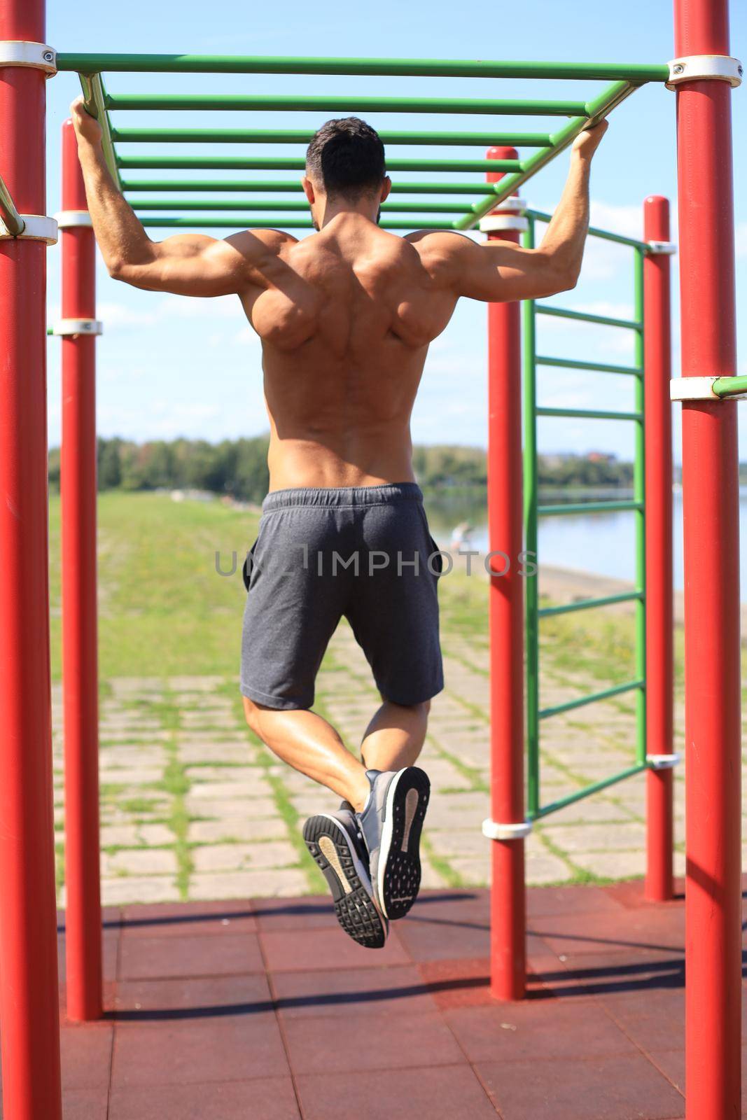 Muscular guy with naked torso pulling up on horizontal bar outdoor by tsyhun