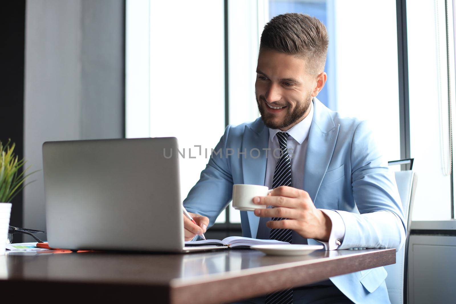 Portrait of happy businessman sitting at office desk, smiling.