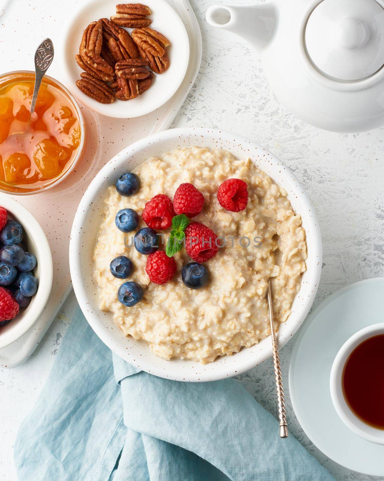 Oatmeal porridge with blueberry, raspberries, jam and nuts in white bowl, dash diet with berries, white background, side view, vertical. Healthy diet breakfast