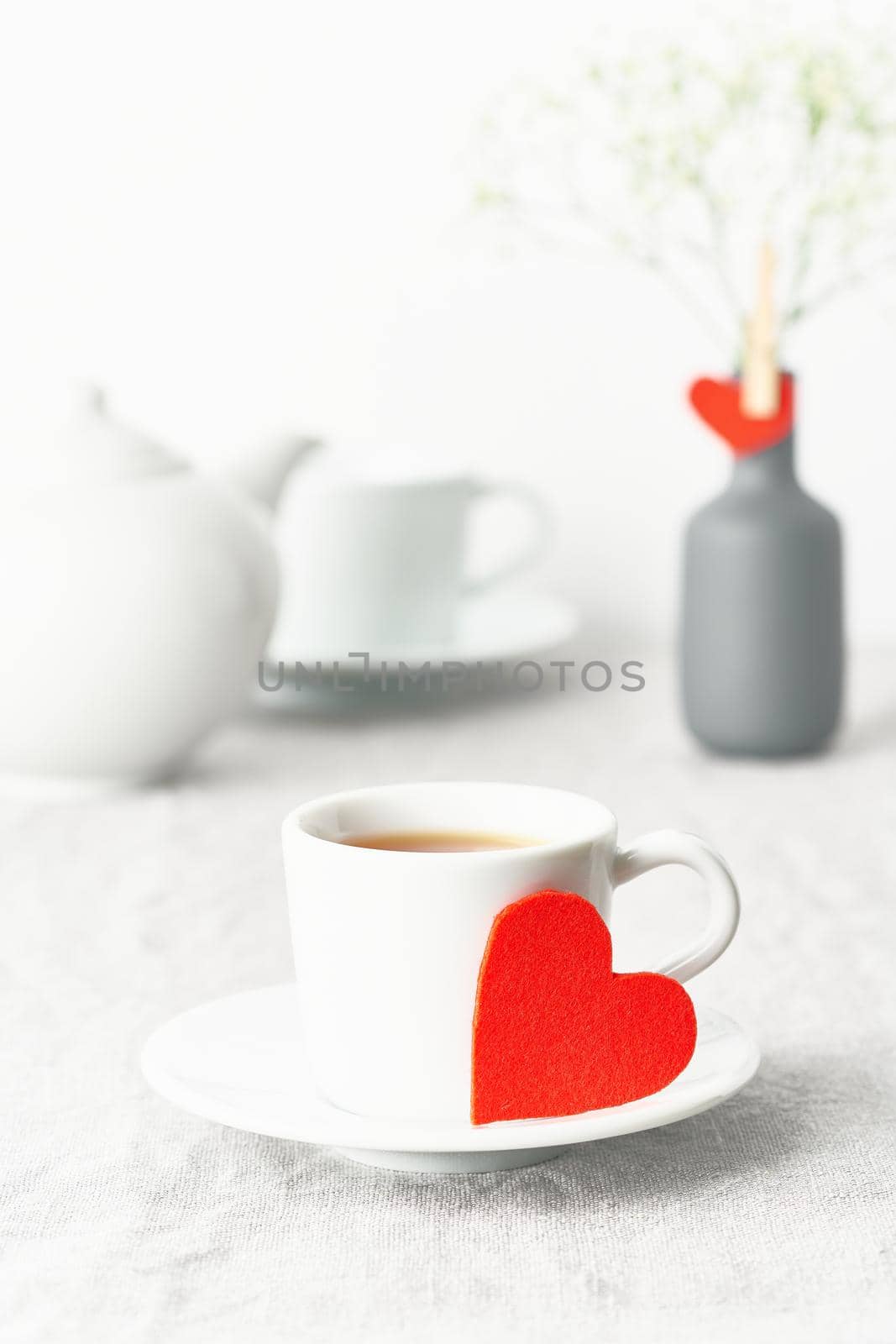 Valentine's Day. Morning breakfast for two with tea and flowers. Red felt heart is symbol of lovers. Light white tender pastel background. Vertical, copy space. Scandinavian minimalism