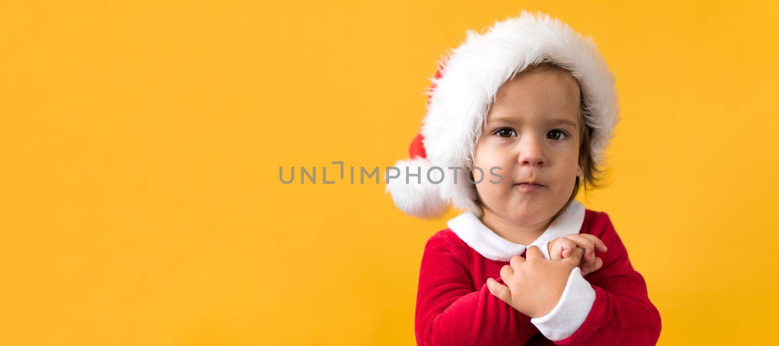 Banner Portraite Cute Happy Cheerful Chubby Baby Girl in Santa Suit Looking On Camera At Yellow Background. Child Play Christmas Scene Celebrating Birthday. Kid Have Fun Spend New Year Time Copy Space.