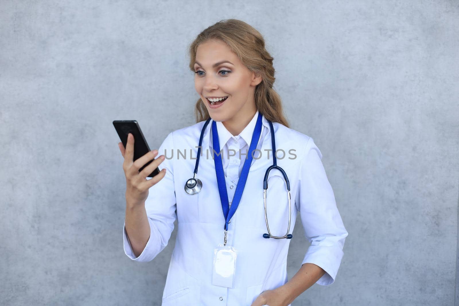 Female doctor smiling and looking in smartphone isolated over grey background