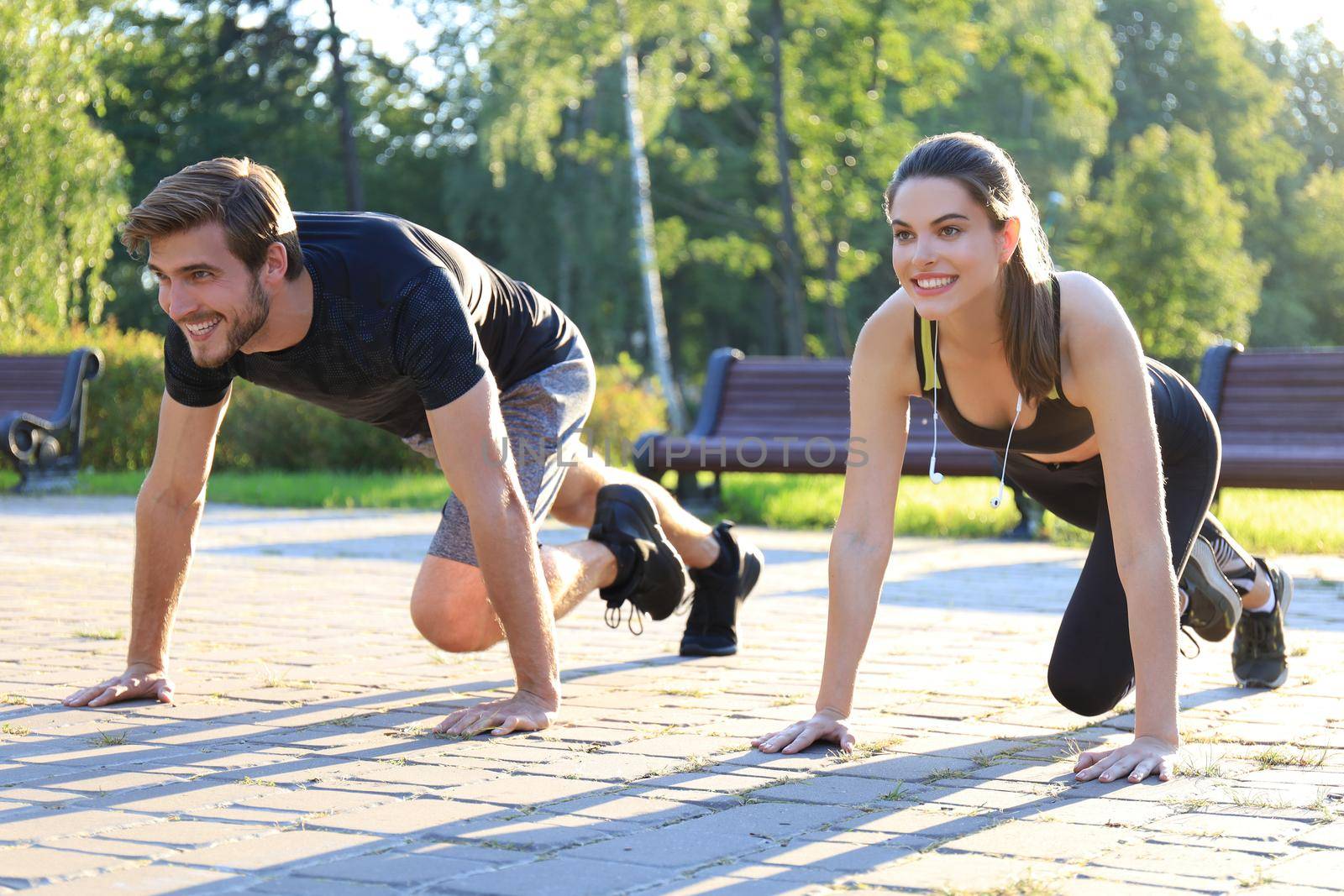 Young couple doing exercise together while working out outdoors in park. by tsyhun