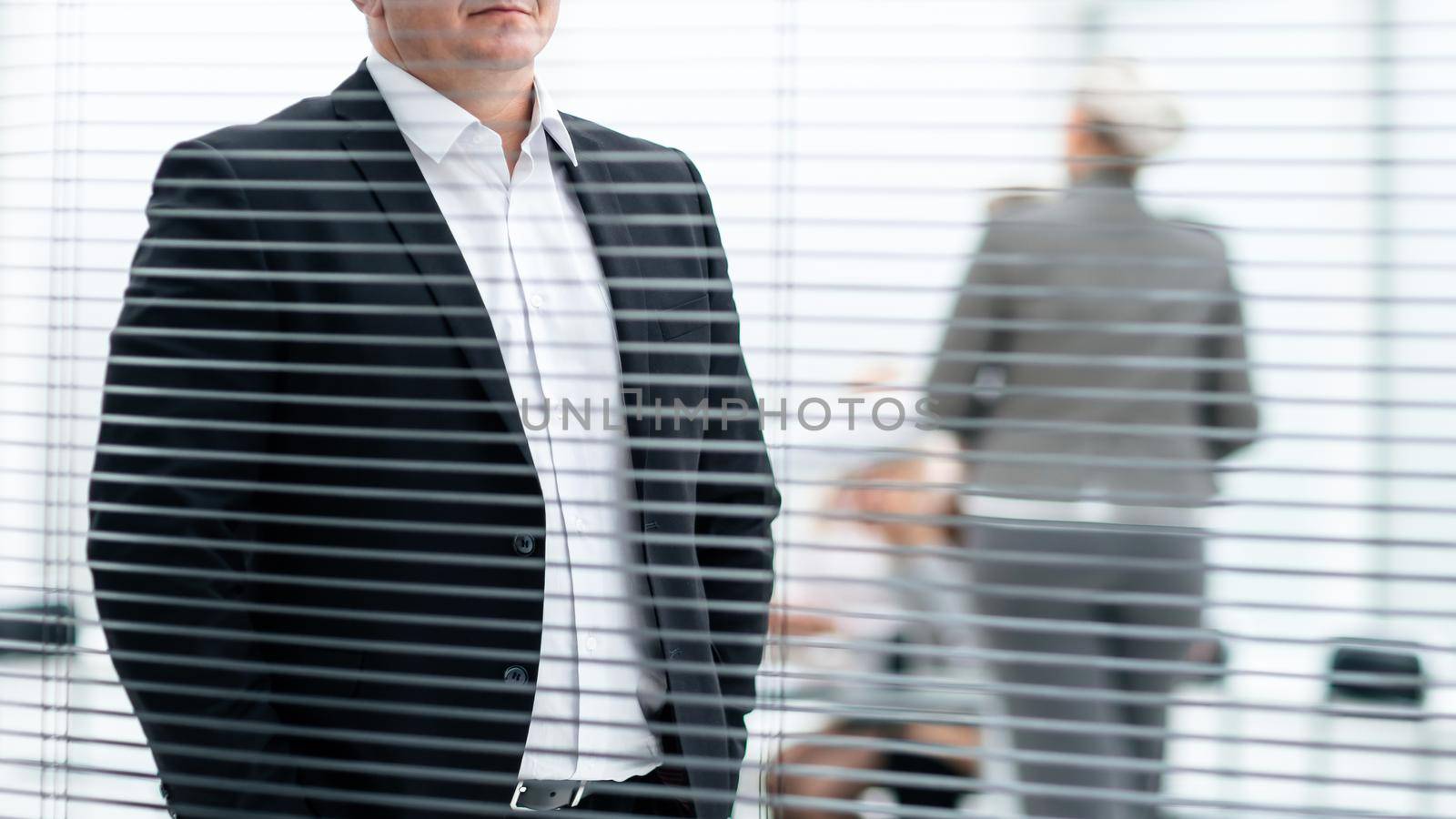 through the blinds. serious business man standing in modern office. business people