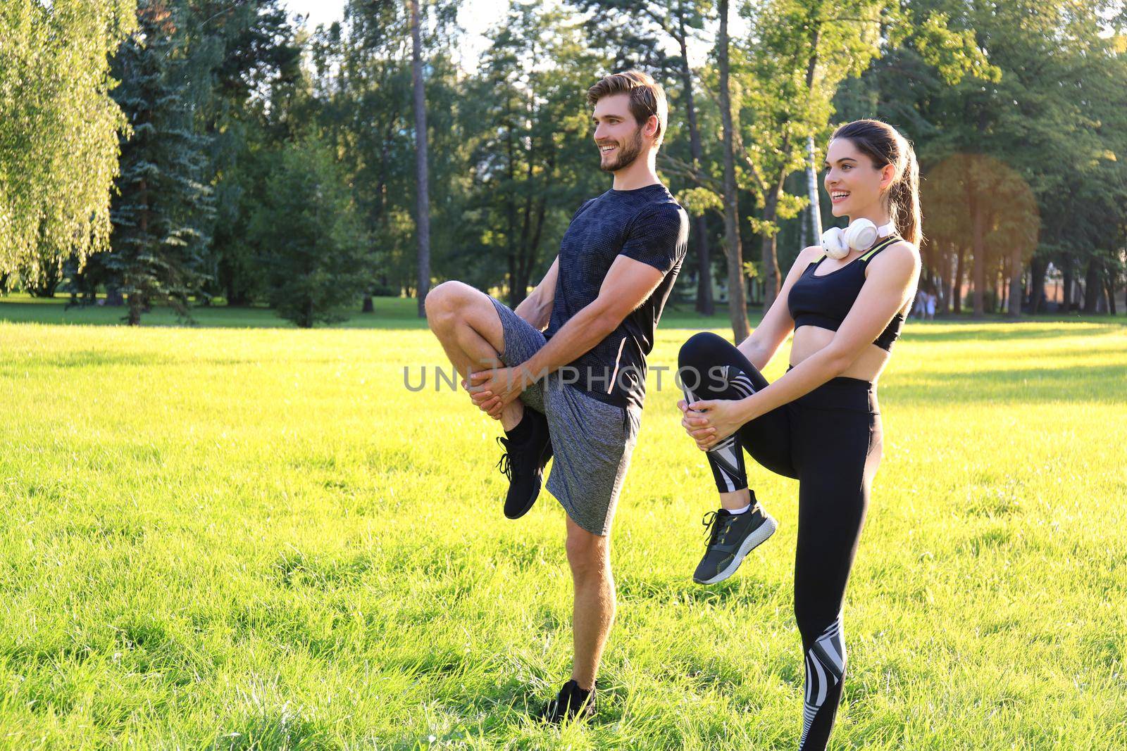 Young couple stretching their legs together while working out at park outdoors