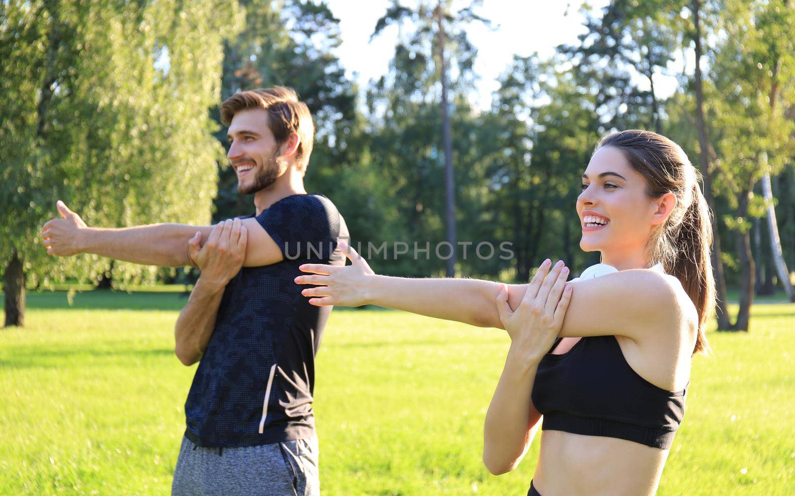 Young couple stretching muscles outdoors in park at sunny day
