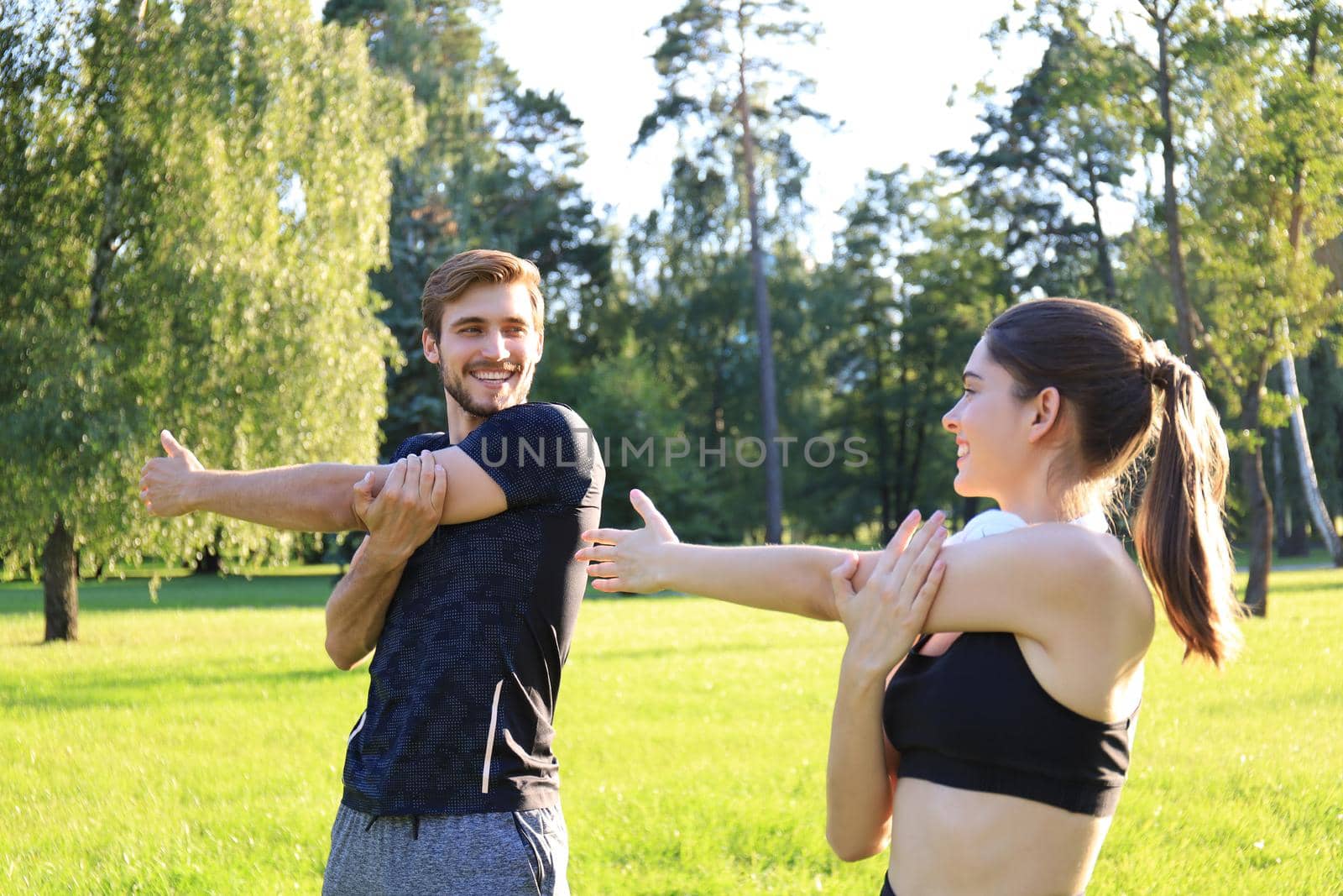 Young couple stretching muscles outdoors in park at sunny day. by tsyhun