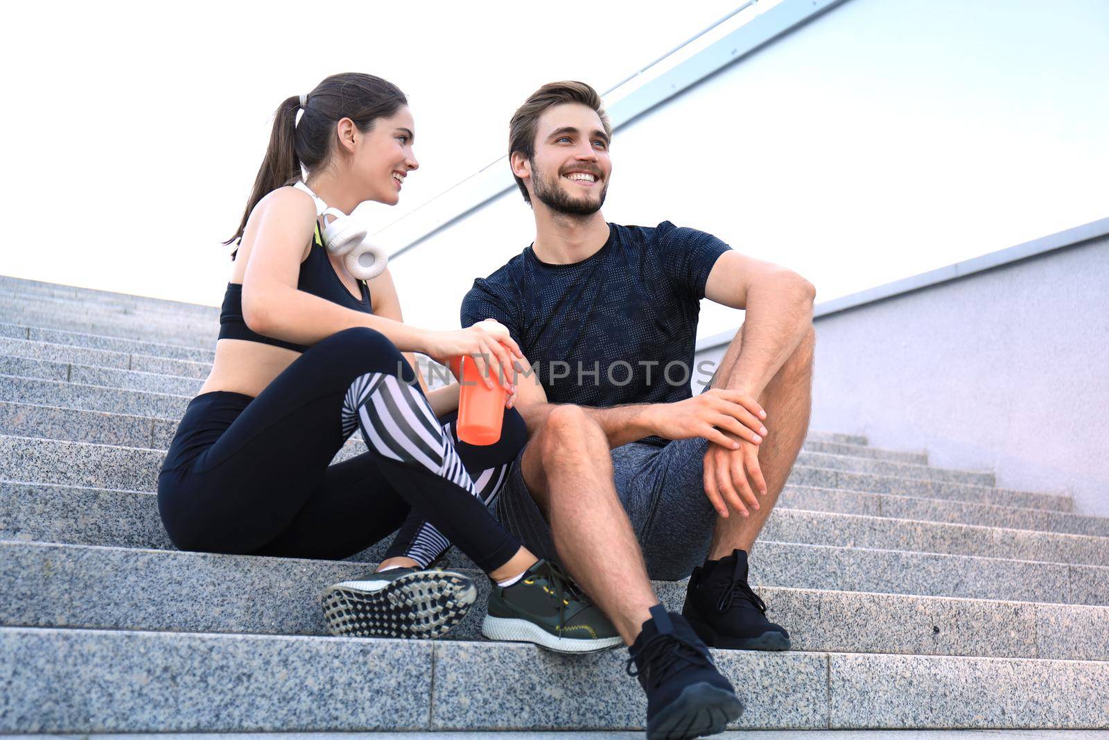 Young couple in sportswear sitting on the stairs after exercising outdoors. by tsyhun