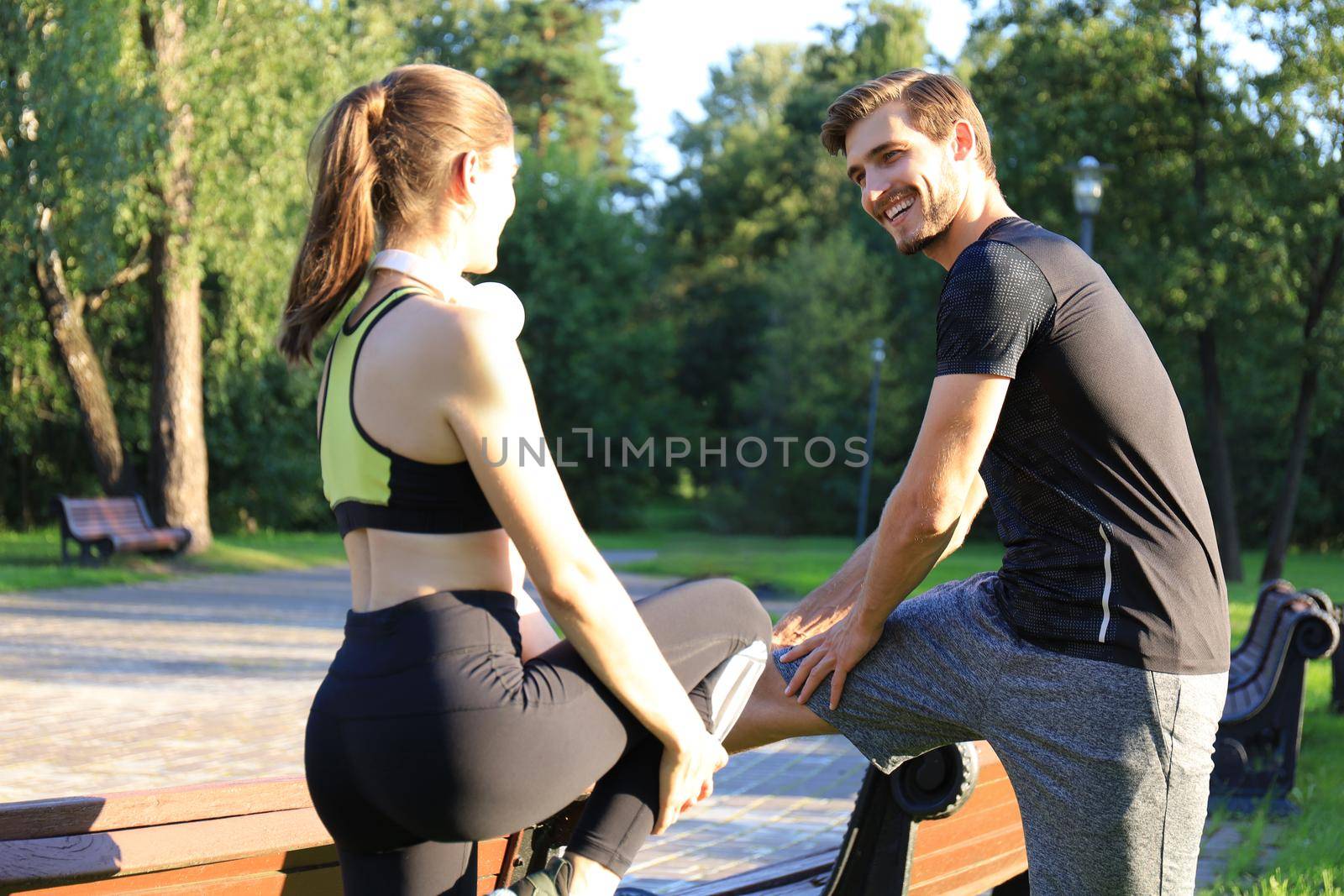 Young couple stretching their legs together while working out at park outdoors. by tsyhun