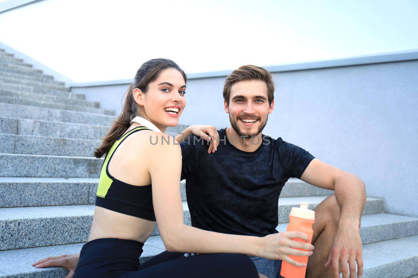 Young couple in sportswear sitting on the stairs after exercising outdoors. by tsyhun