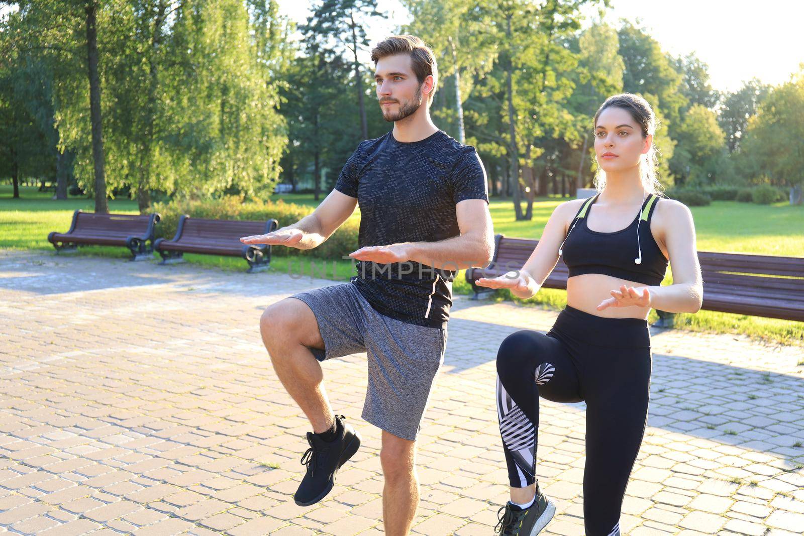 Young couple doing exercise together while working out outdoors in park. by tsyhun