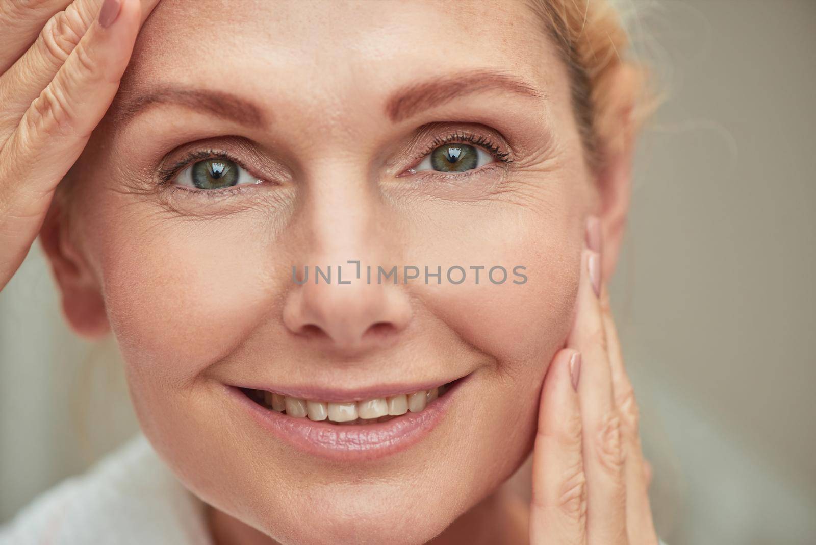 Portrait of beautiful middle aged caucasian woman holding hands near face while looking at camera during wellness procedure, horizontal shot. Beauty, skincare and cosmetology concept