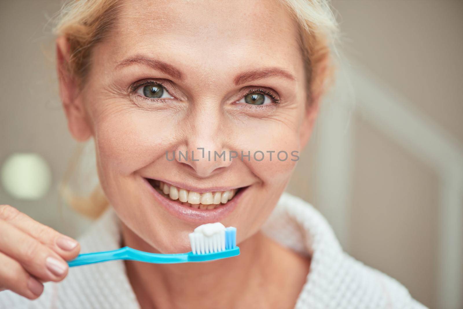Portrait of happy middle aged caucasian woman with toothbrush in hand looking at camera and smiling. Beauty, skincare and cosmetology concept