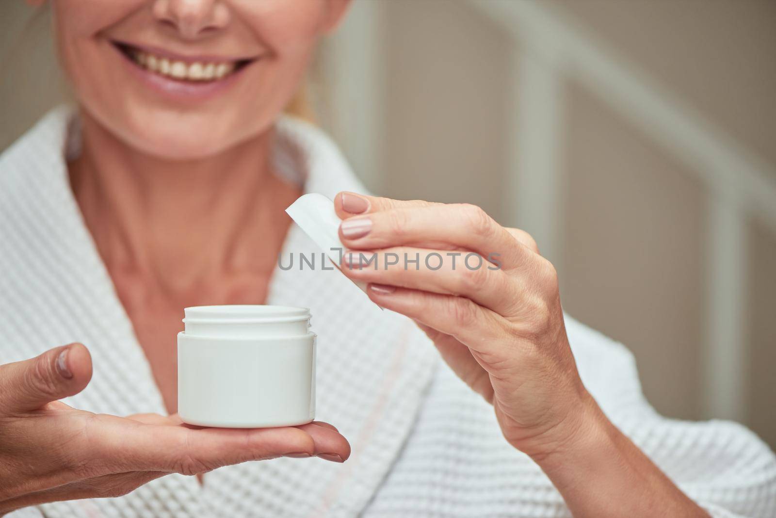 Open cosmetic cream bottle on woman's palm during spa procedure, cropped. Beauty, skincare and cosmetology concept