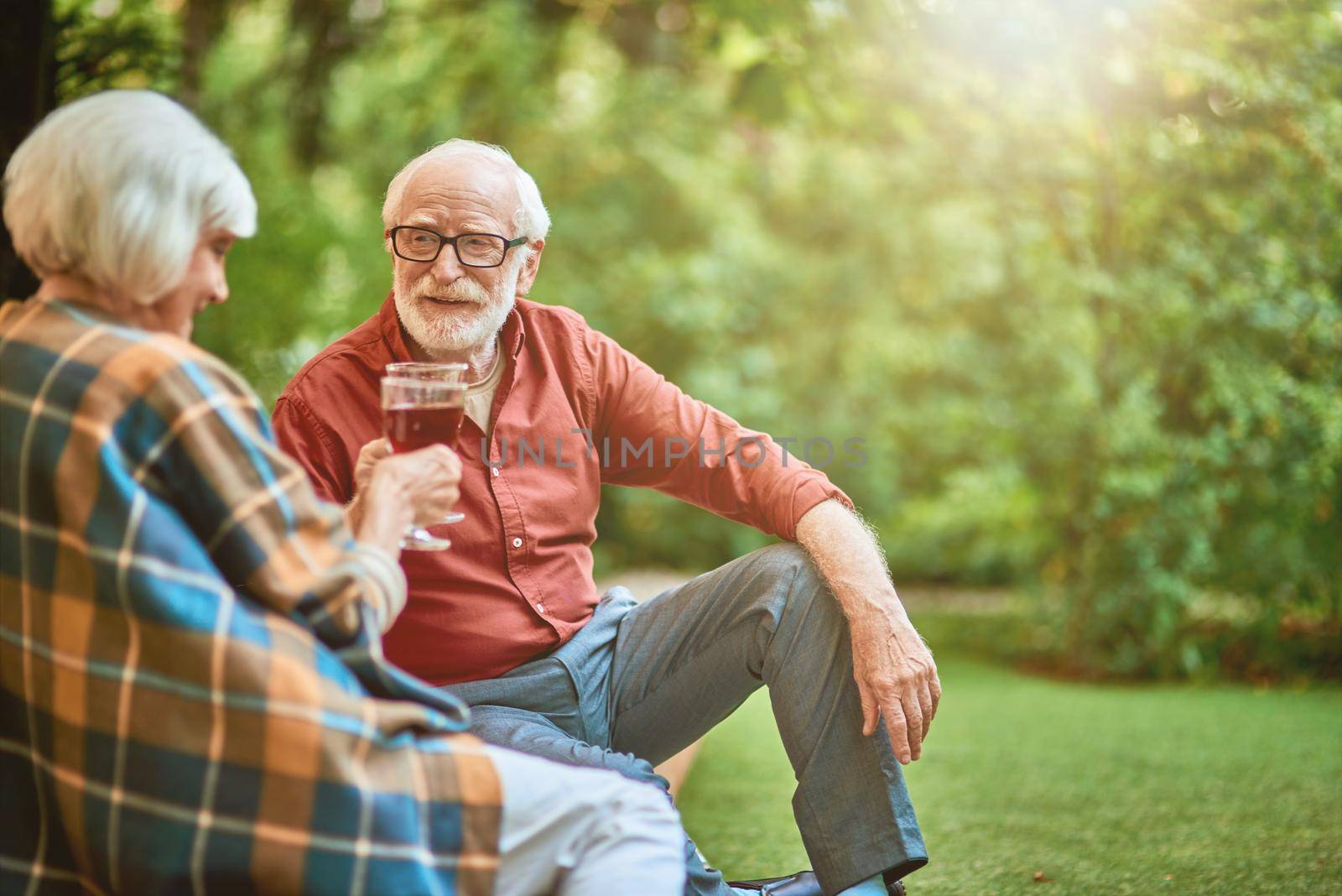 Happy senior man looking at his wife while holding glasses with red wine outdoors. Relationship and family concept. Copy space