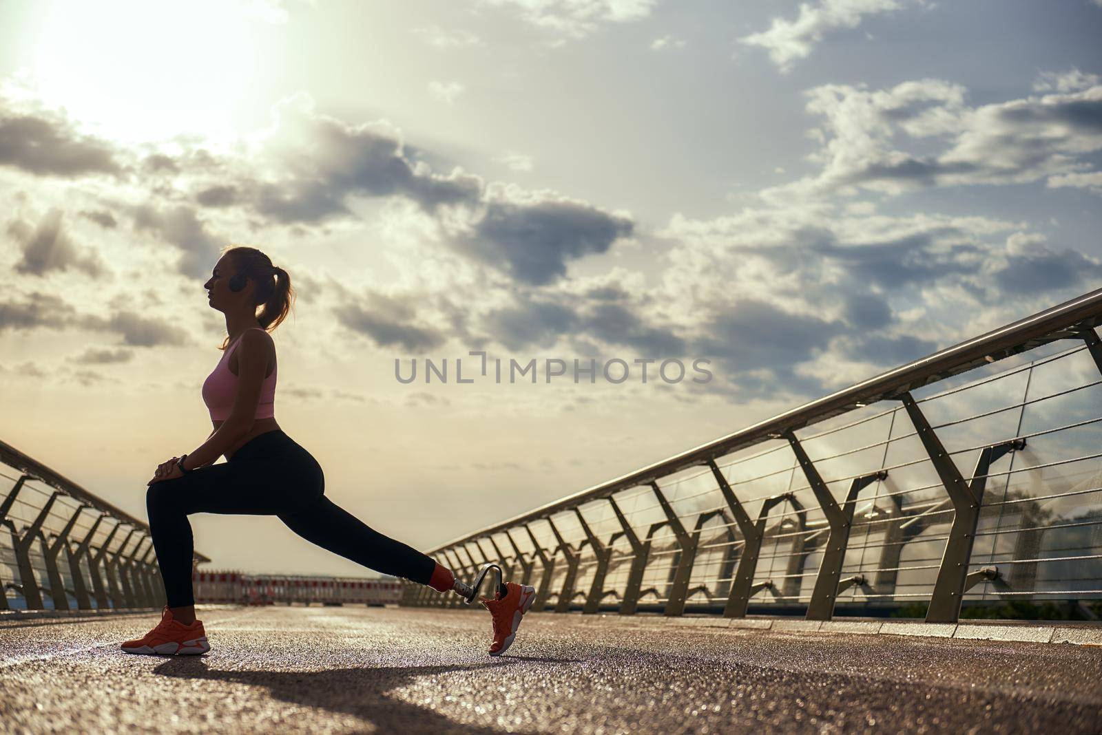 Staying healthy. Full-length of young disabled woman with leg prosthesis in sportswear doing yoga exercises outdoors by friendsstock