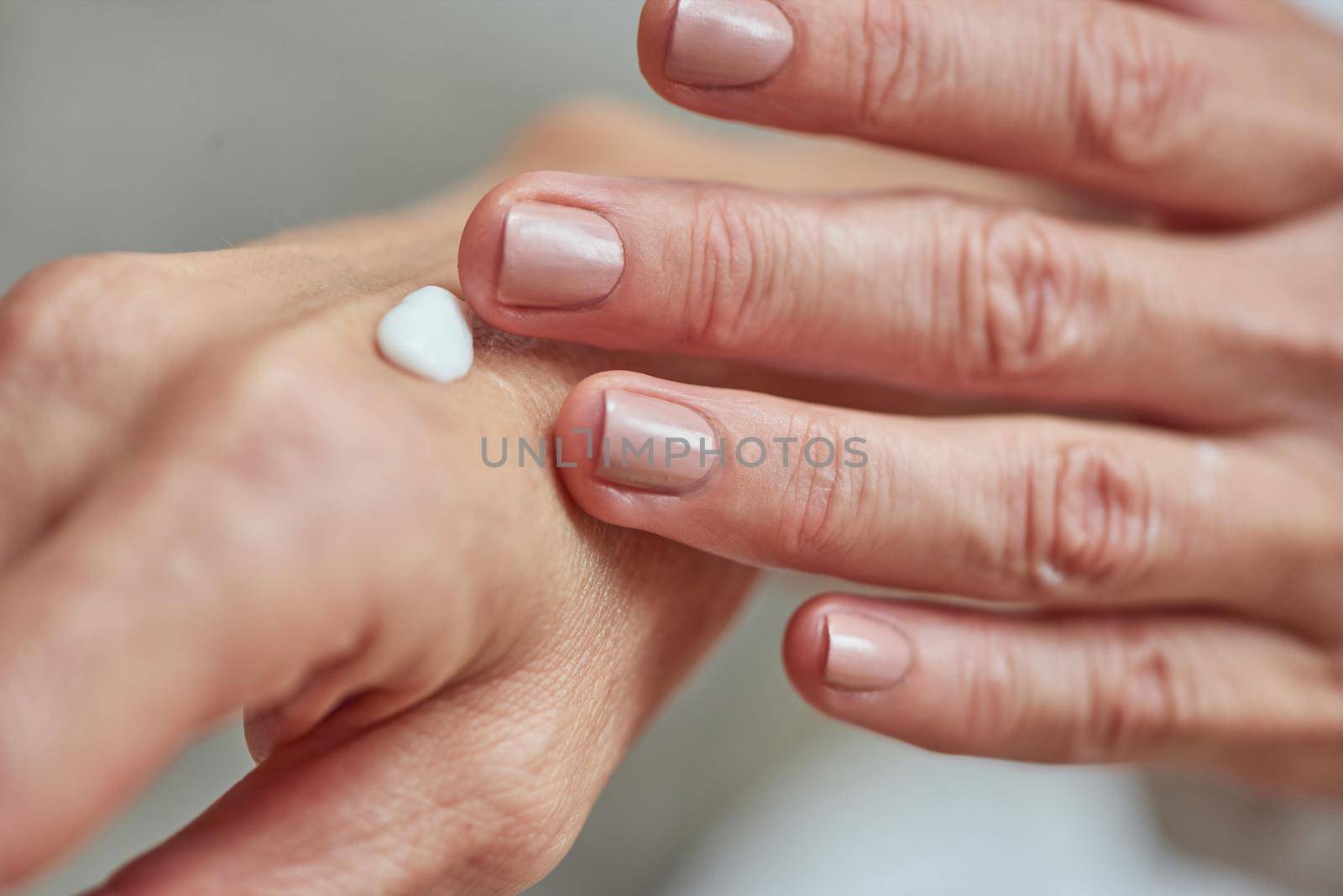 Manicured hands of middle aged woman applying white cream, close up view. Beauty, skincare and cosmetology concept