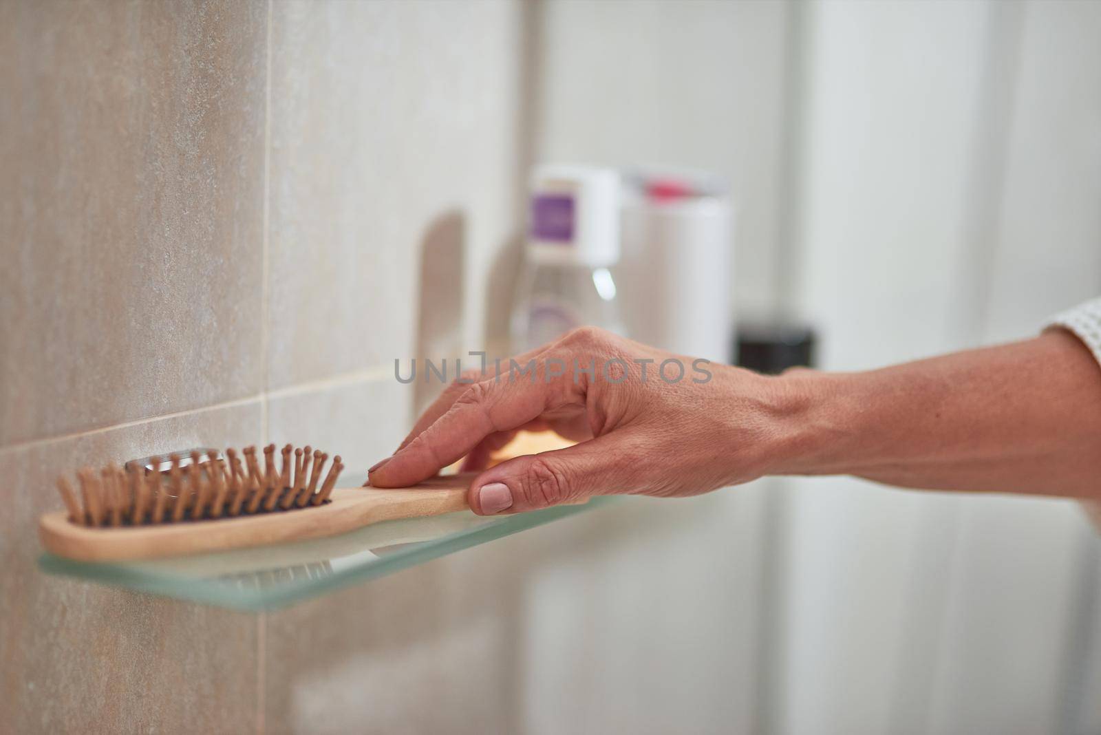 Female hand taking wooden hair brush from bath shelf, selective focus. Beauty, skincare and cosmetology concept