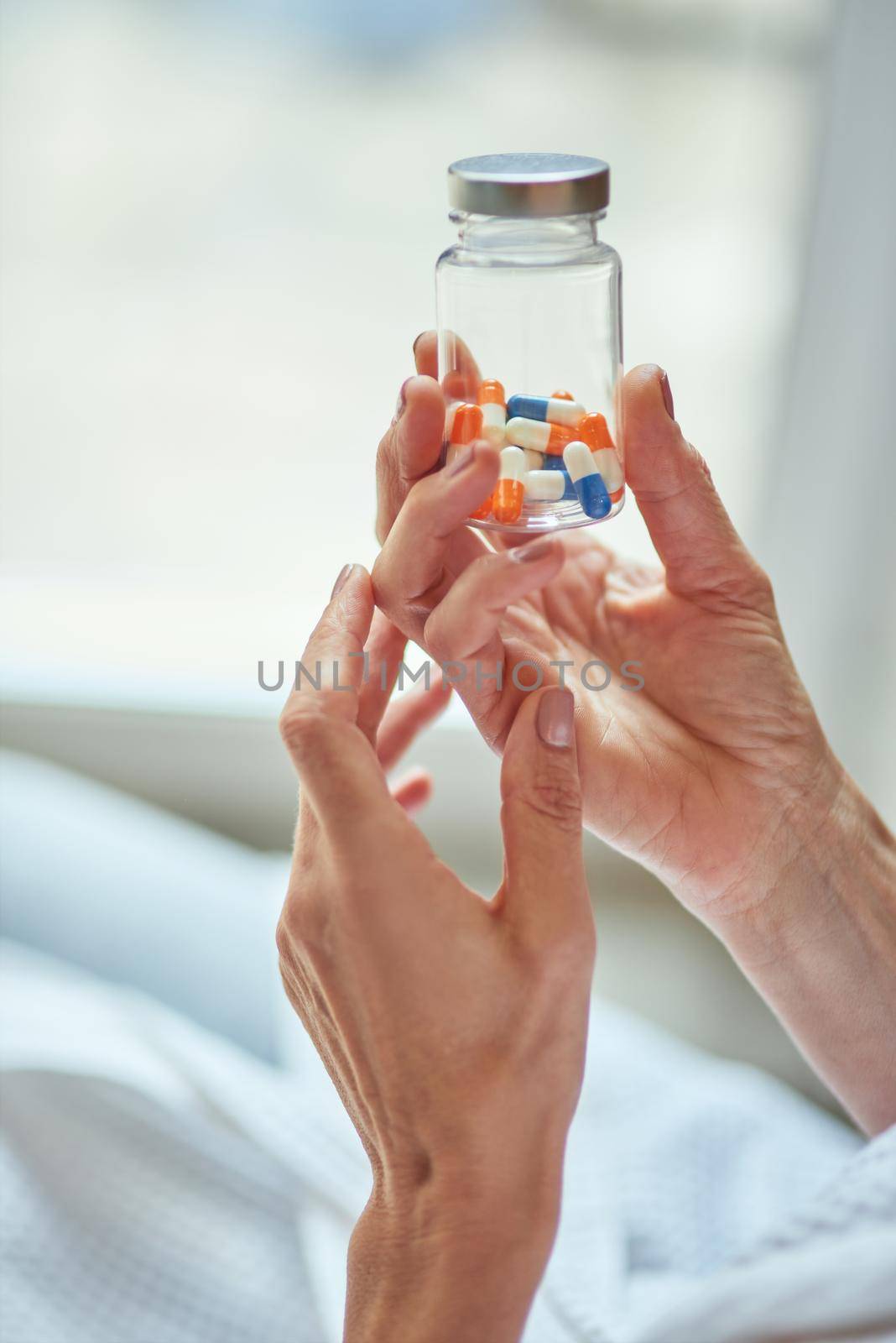 Manicured female hands holding pills in glass bottle on light room background. Beauty and cosmetology concept