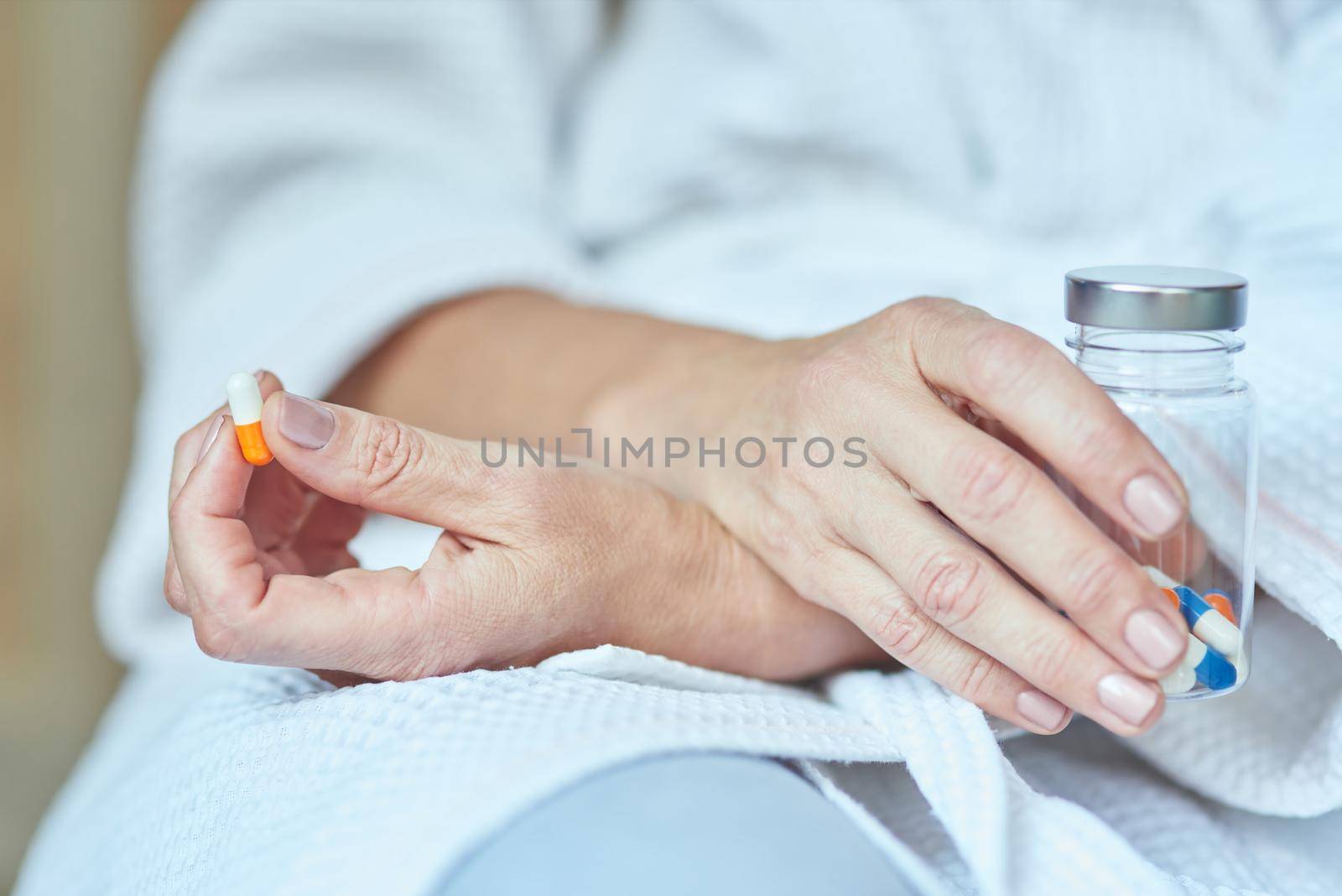Woman sitting with crossed hands holding pill and pill bottle in manicured fingers, close up view of hands. Beauty and cosmetology concept