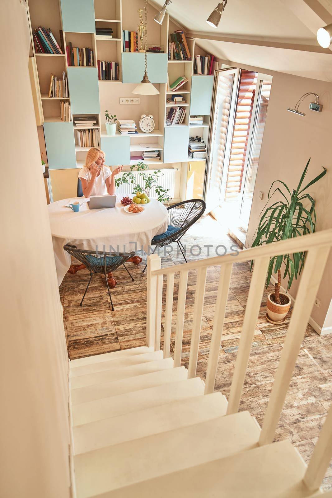 Middle aged caucasian business woman working at home sitting at kitchen table viewed from downstairs. Working from home concept