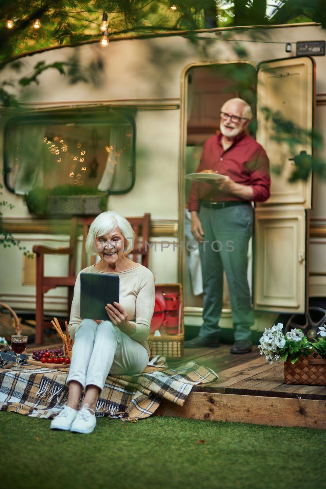 Happy elderly lady holding gadget while sitting on the van porch by friendsstock