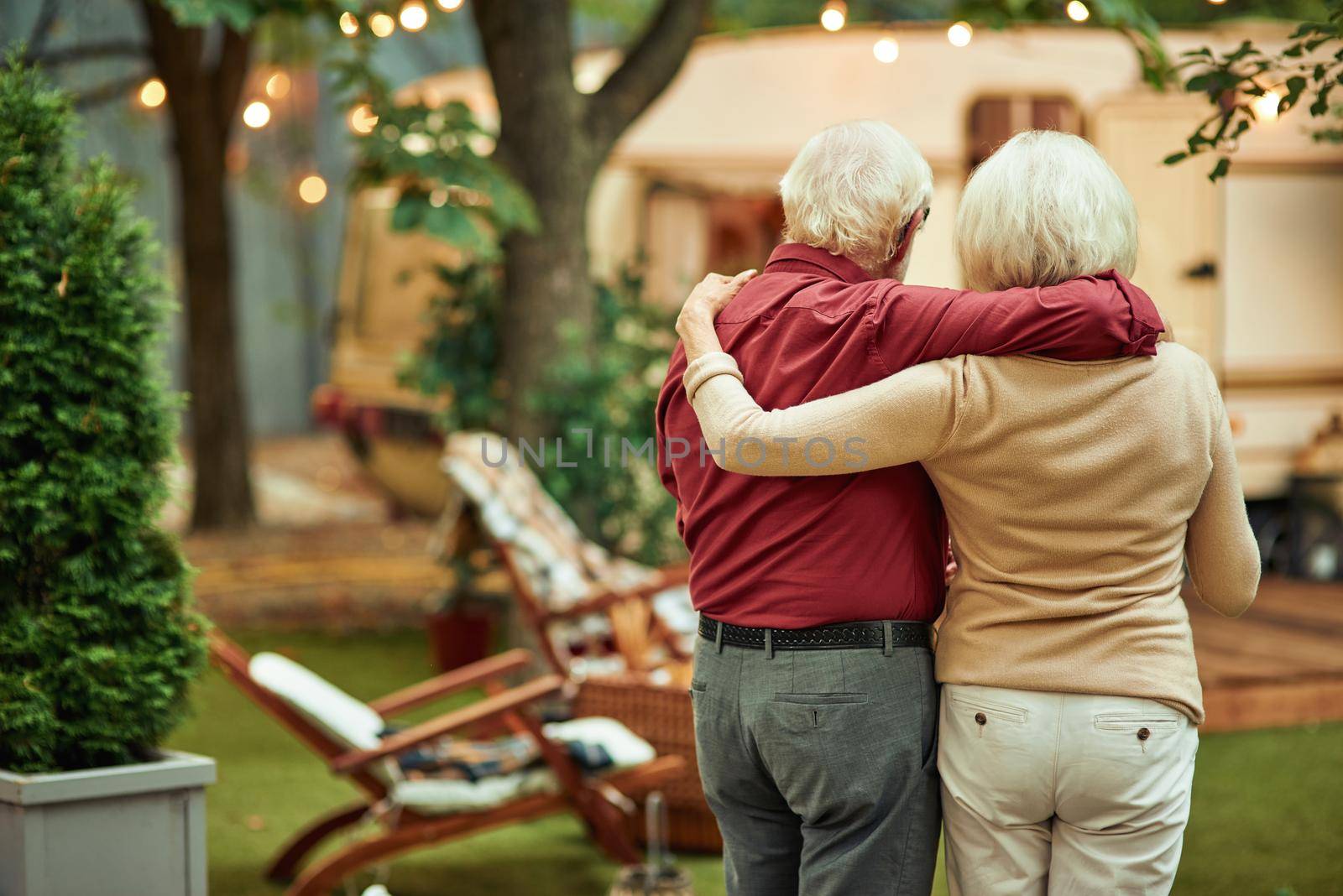Back view of elderly couple hugging outdoors with their motorhome on the background. Travel concept. Copy space
