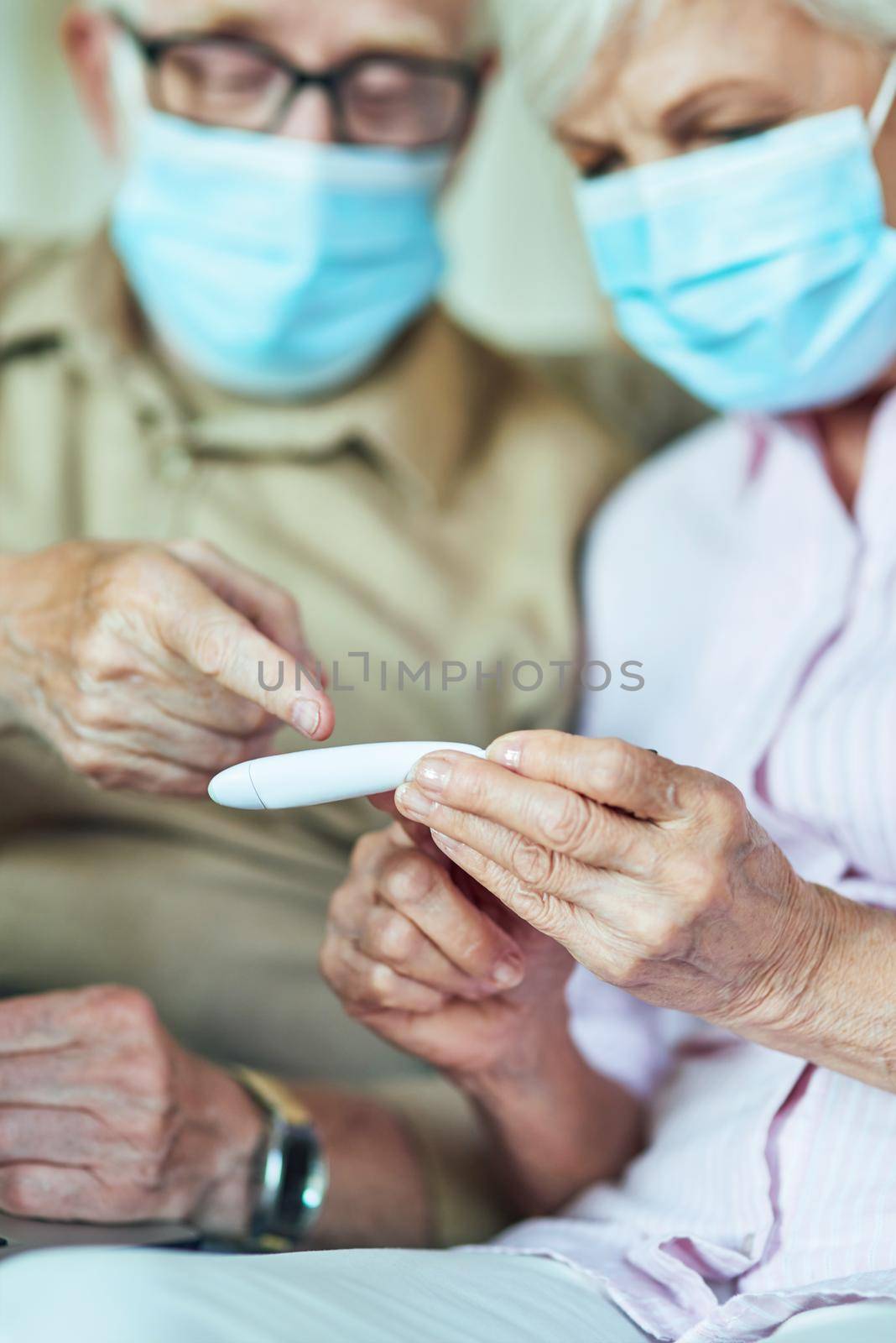 Close up of elderly couple wearing protective mask and checking the temperature at home. Care and health concept