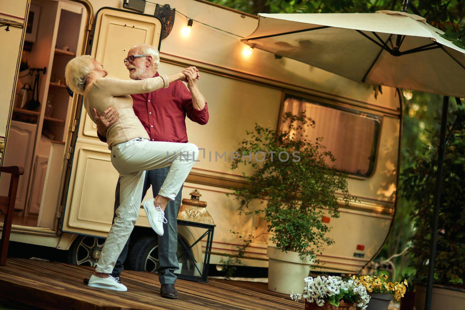 Full length photo of happy senior couple dancing while staying on the van porch evening. Travel concept