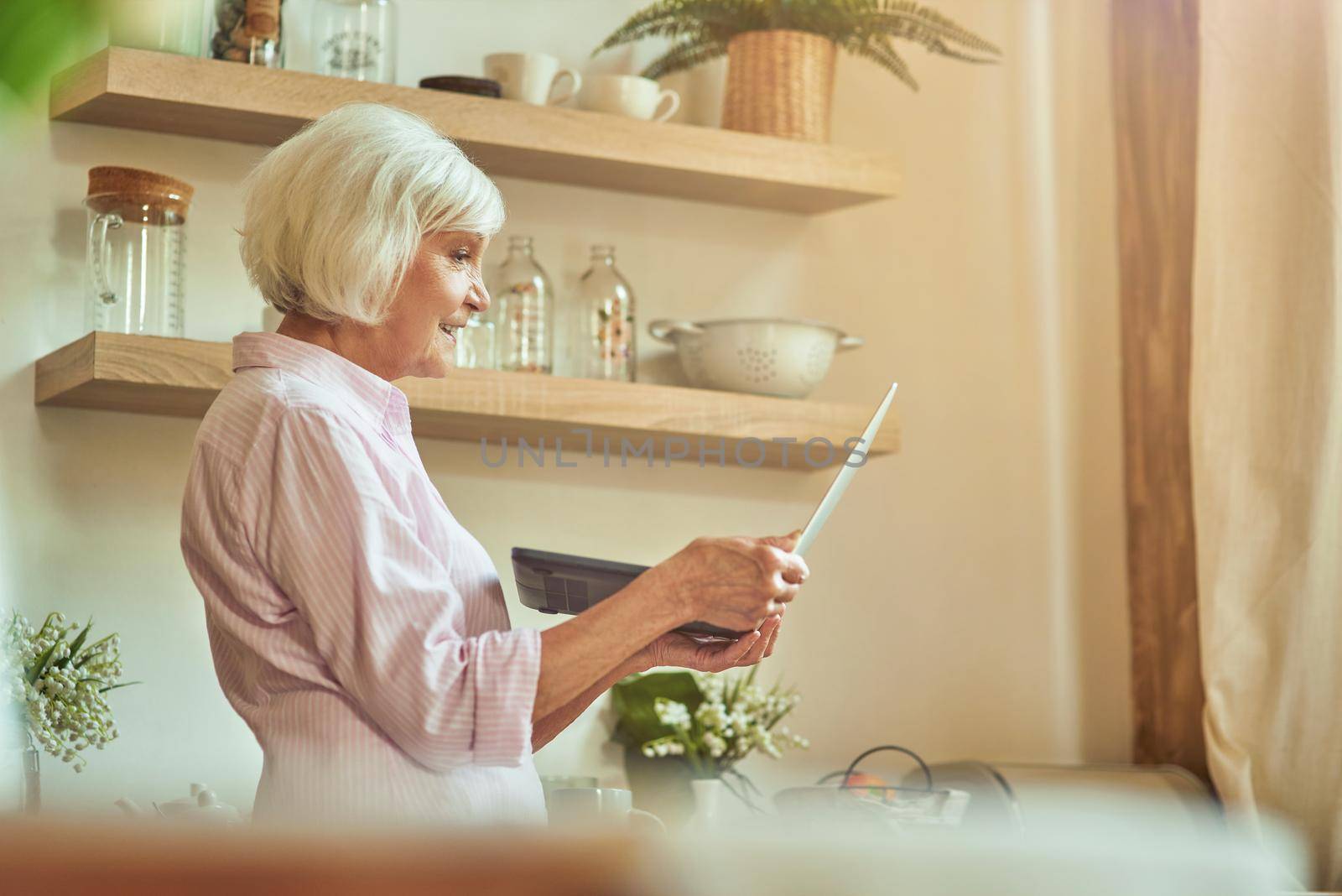 Smiling elder woman using gadget at her home by friendsstock