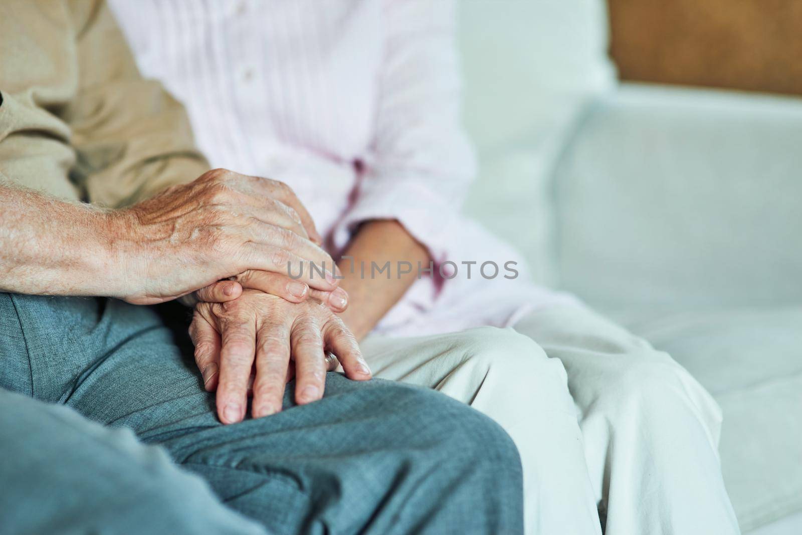 Close up of elderly hands of couple sitting on the sofa at home. Family and relationships concept