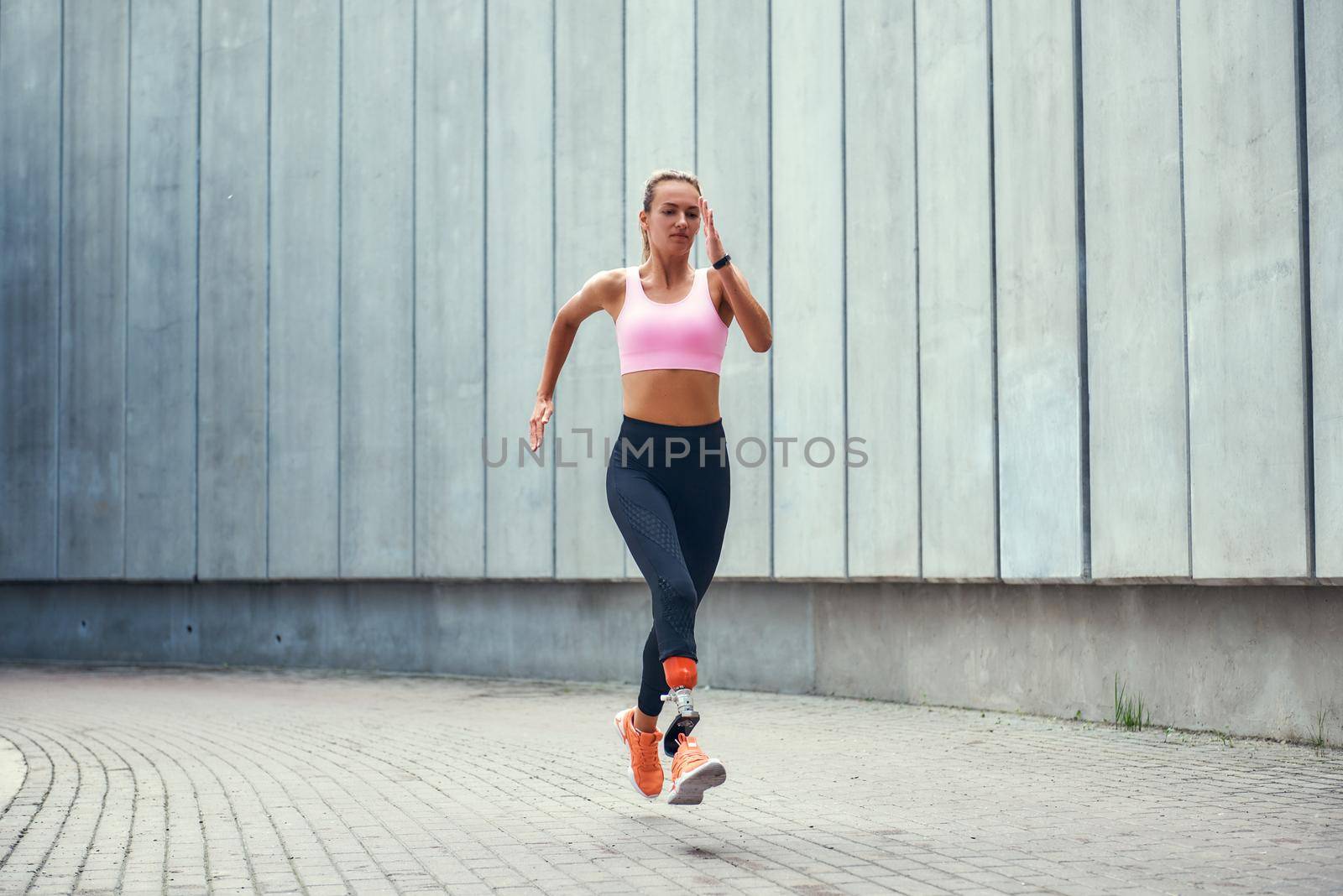My motivation. Full-length of young disabled woman with leg prosthesis in comfortable sports clothing is running outdoors along the street by friendsstock