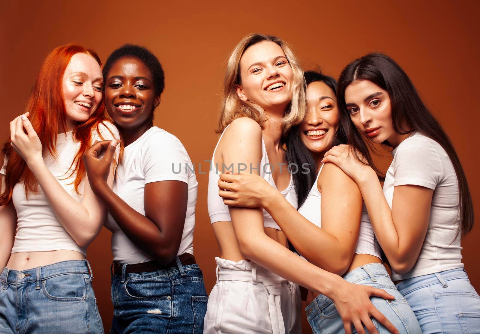 young pretty african and caucasian women posing cheerful together on brown background, lifestyle diverse nationality people concept close up