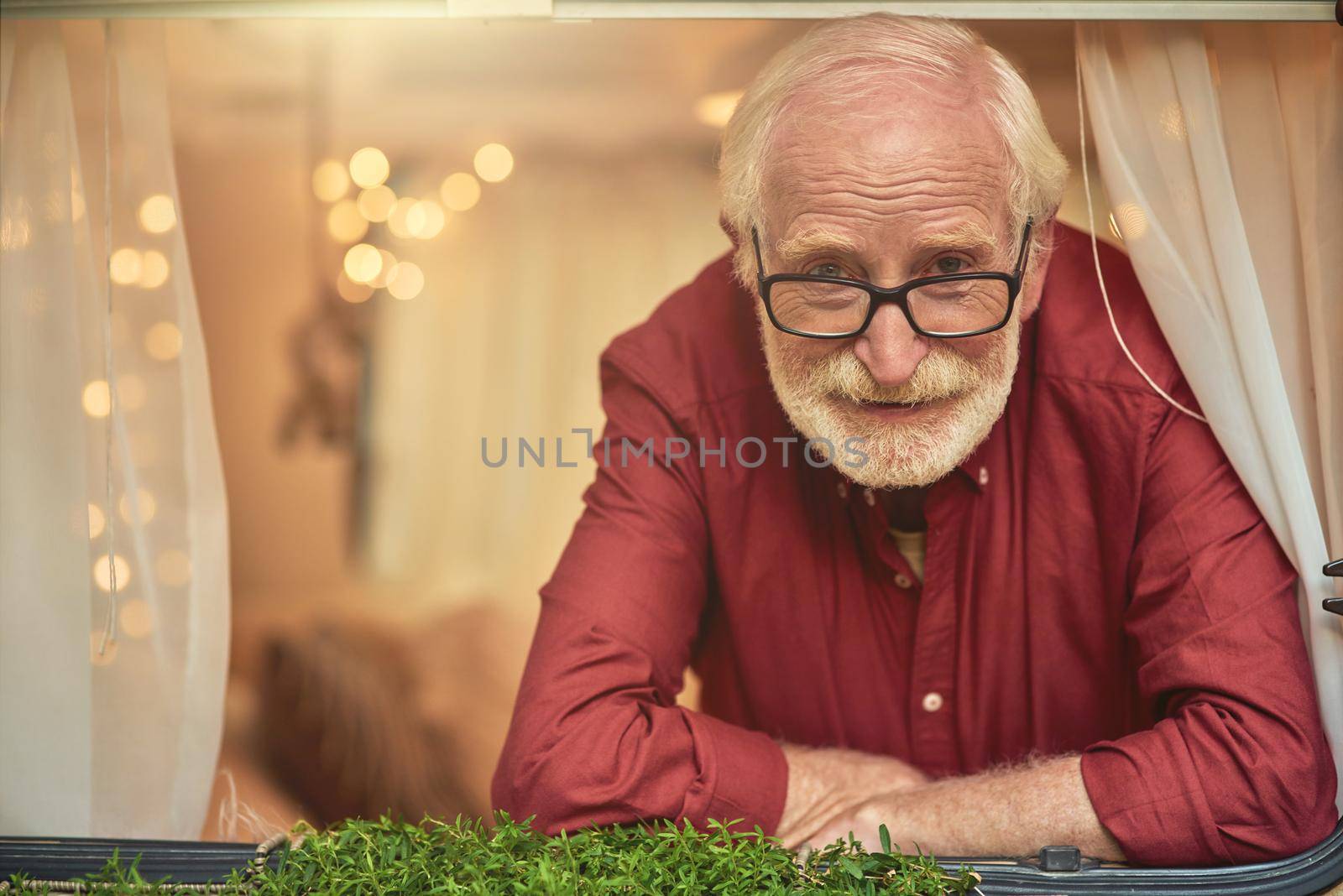 Portrait of happy man with wrinkles wearing glasses and looking in the motorhome window. Travel concept. Copy space