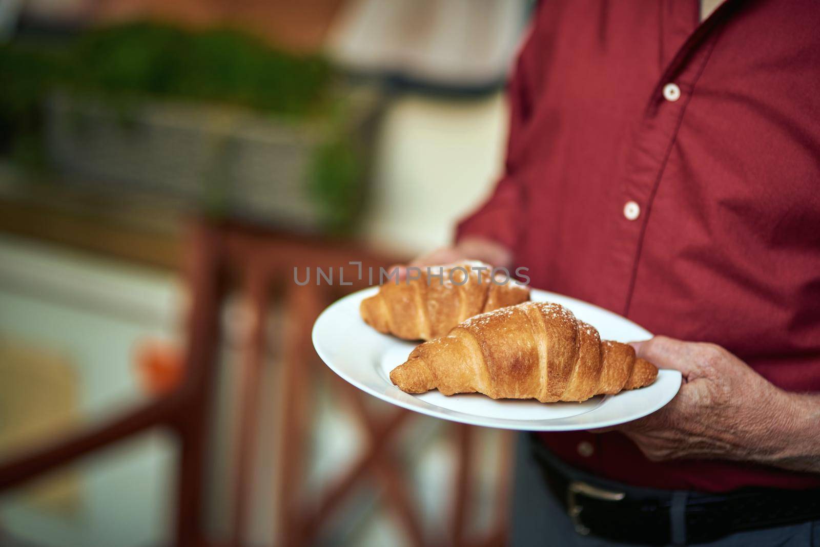 Cropped photo of male hands holding holding a plate with two croissants while standing outdoors. Lifestyle concept. Copy space
