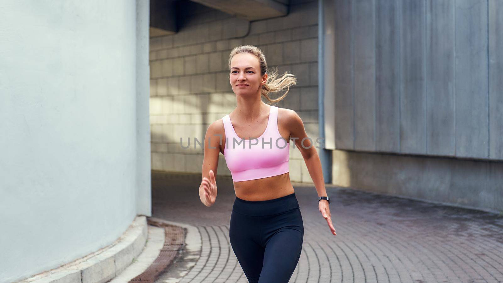 Enjoying run. Young smiling woman in comfortable sports clothing is running outdoors along the street by friendsstock
