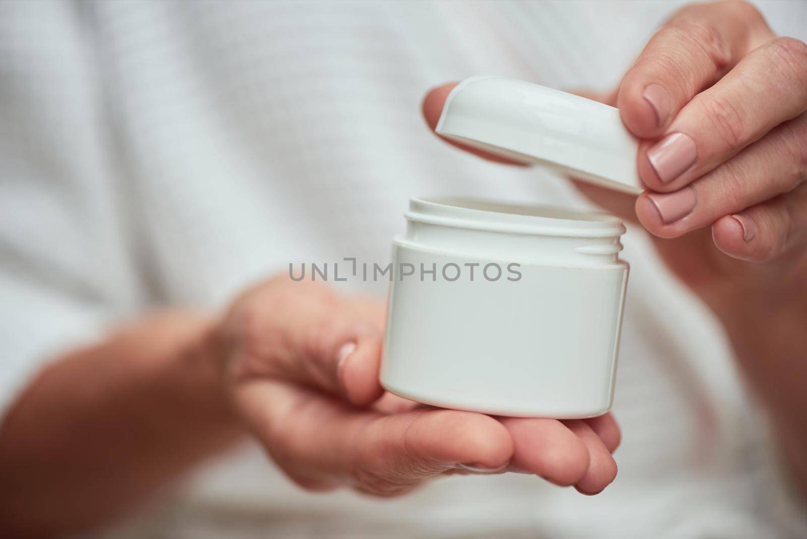 Close up view of woman opening cosmetic cream bottle with manicured hands. Beauty, skincare and cosmetology concept