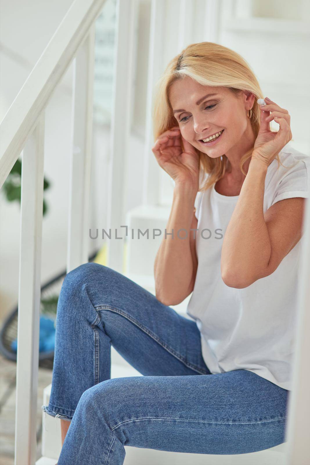 Middle aged caucasian woman sitting on stairs with earphones by friendsstock