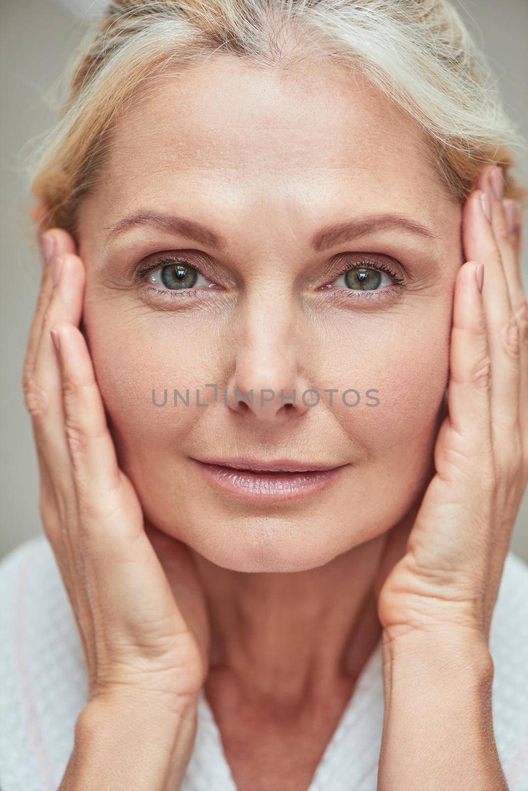 Portrait of beautiful middle aged caucasian woman looking at camera with hands near face, close up. Beauty, skincare and cosmetology concept