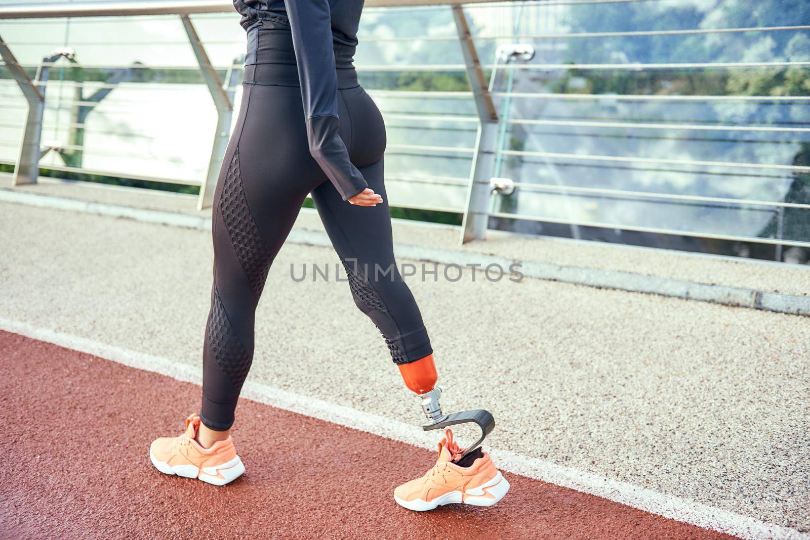 Cropped photo of disabled athlete woman with prosthetic leg in sportswear walking on the bridge. Disabled sport concept. Motivation. Healthy lifestyle