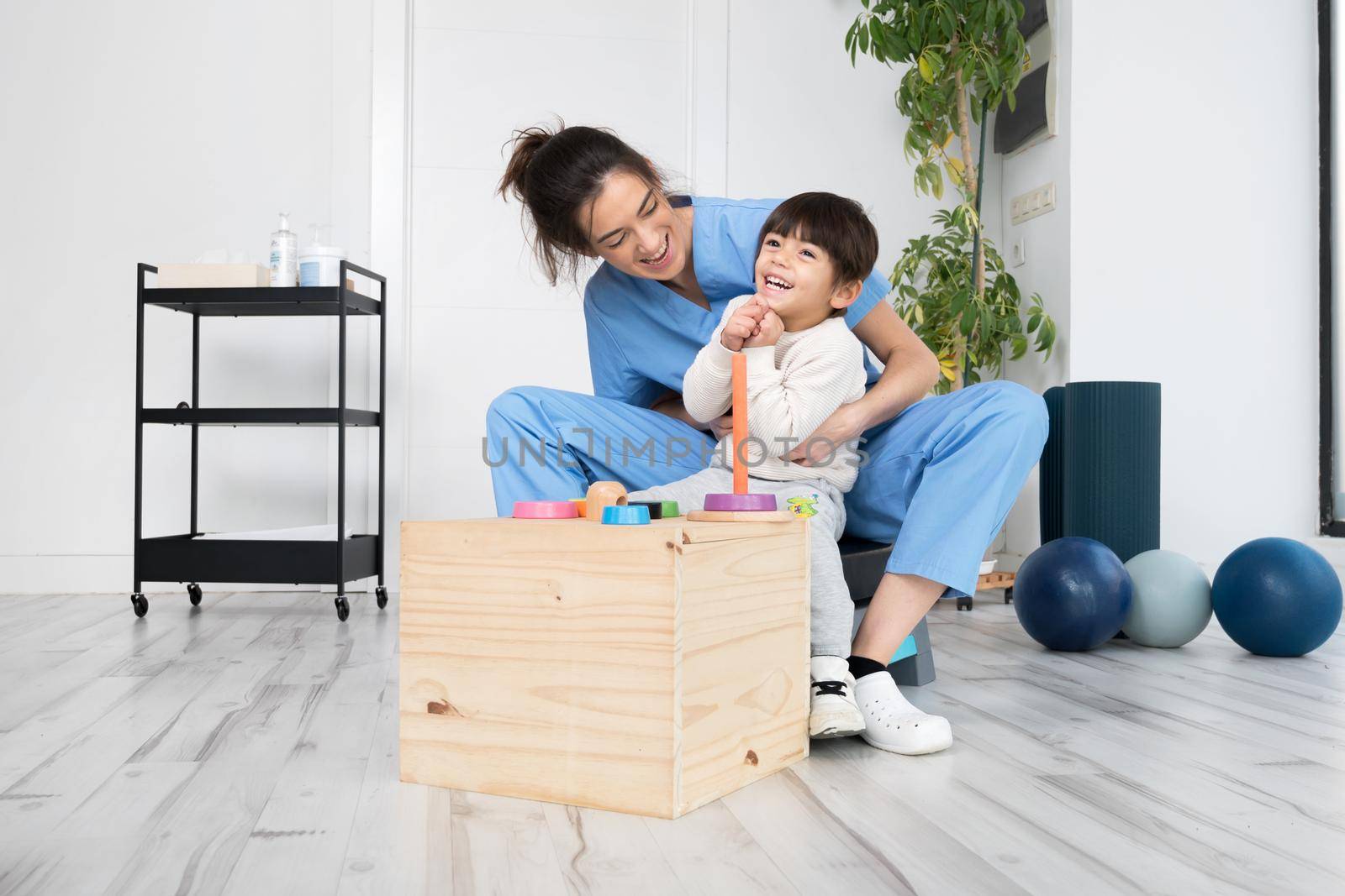 Therapist doing development activities with a little boy with with cerebral palsy, having rehabilitation, learning . Training in medical care center by HERRAEZ