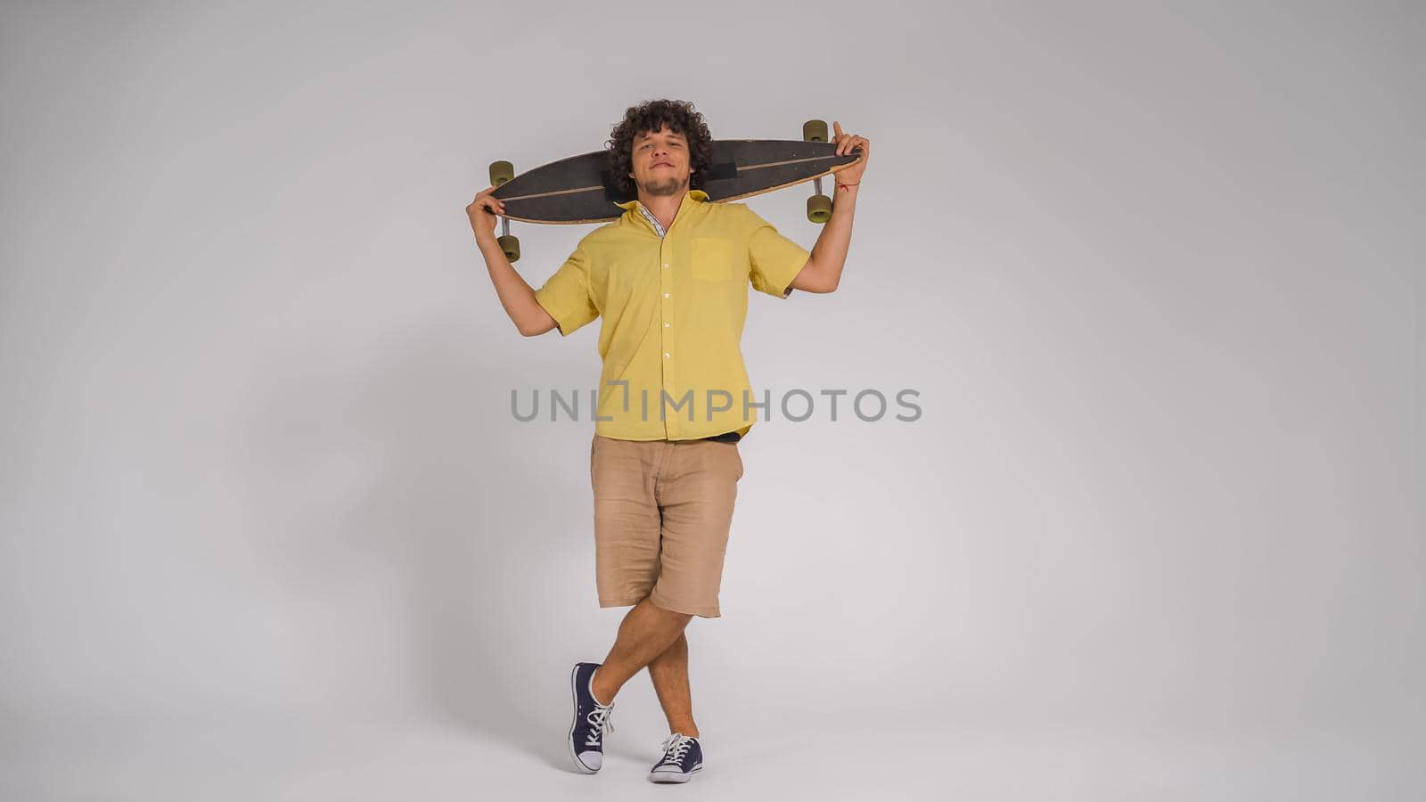 Happy guy holds longboard on his shoulders looking into the camera. Cut out on white background. Full length shot. Lifestyle concept.