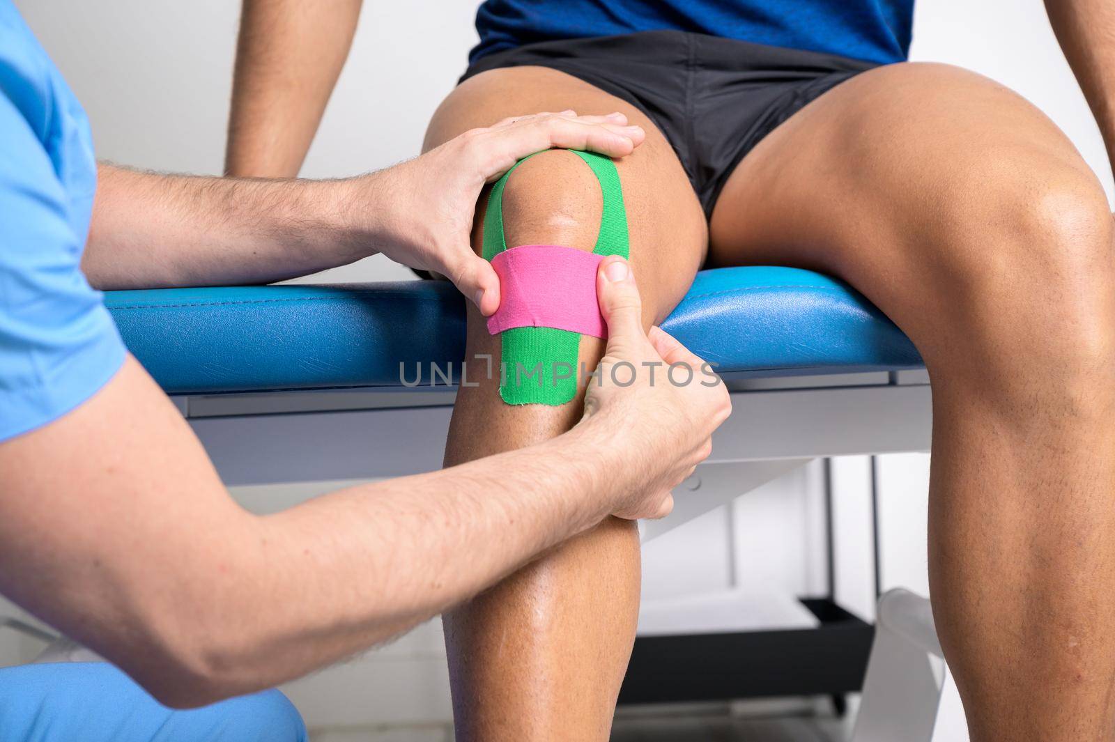 Physical therapist applying kinesio tape on male patient knee. Kinesiology, physical therapy, rehabilitation concept. close up by HERRAEZ