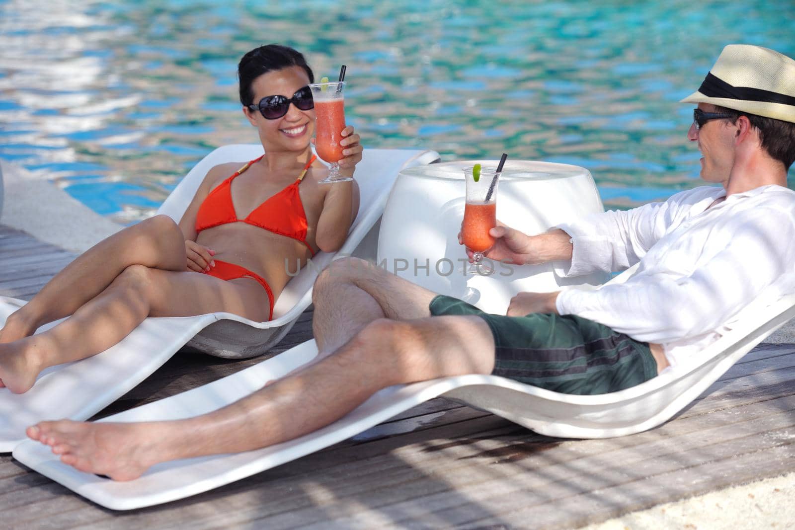happy young couple relax and take fresh drink on poolside by dotshock