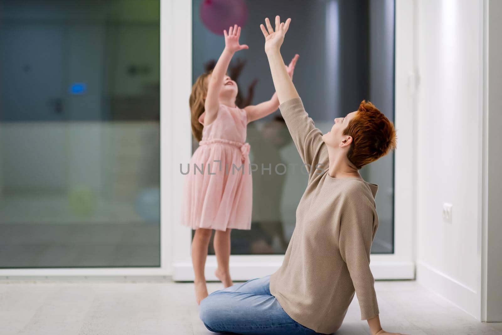 happy family spending time together young redhead mother and cute little daughter having fun while playing with balloons near the window on beautiful evening at home