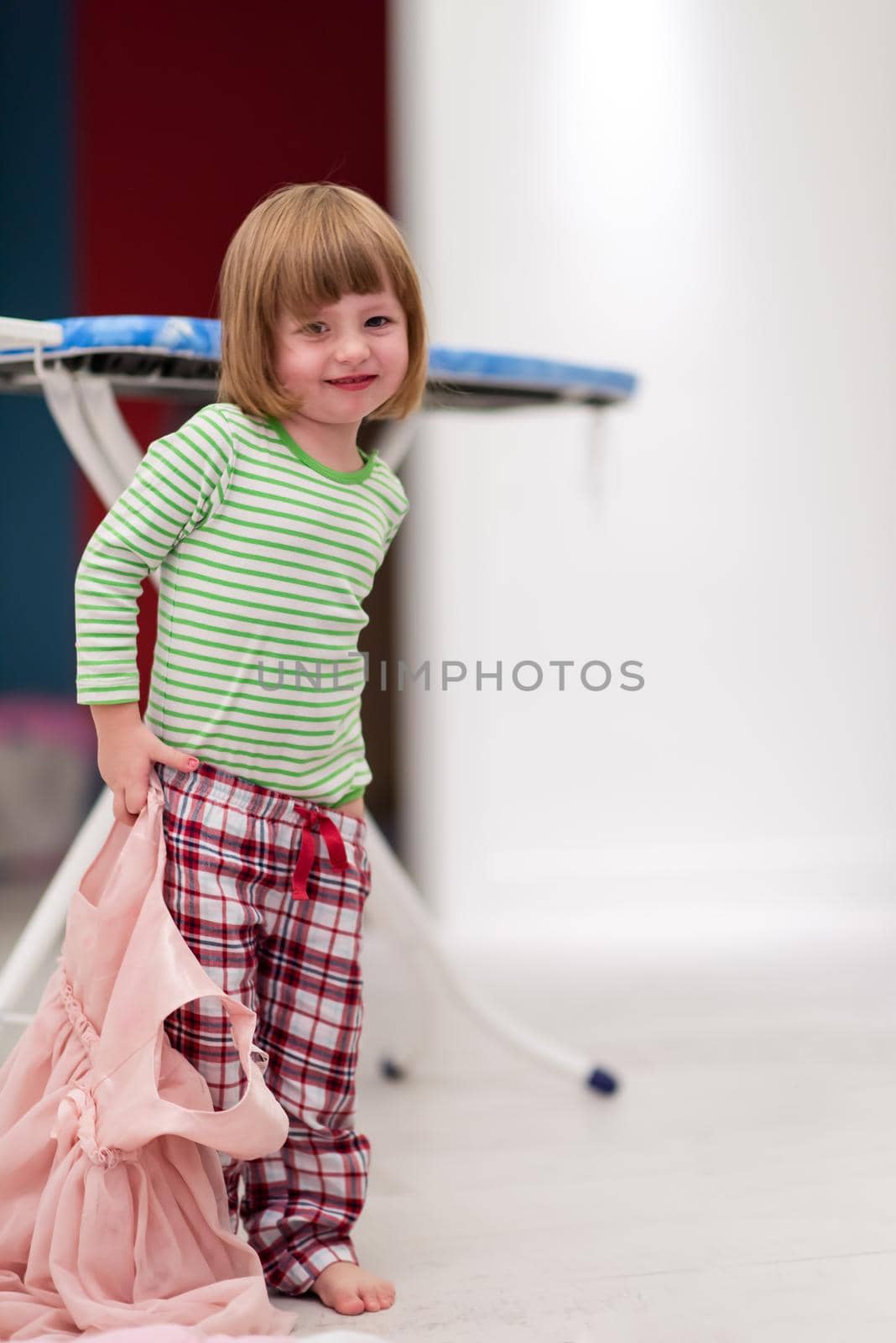 portrait of a cute little girl with a pink dress in her hand that she wants to put on herself at stylish apartment