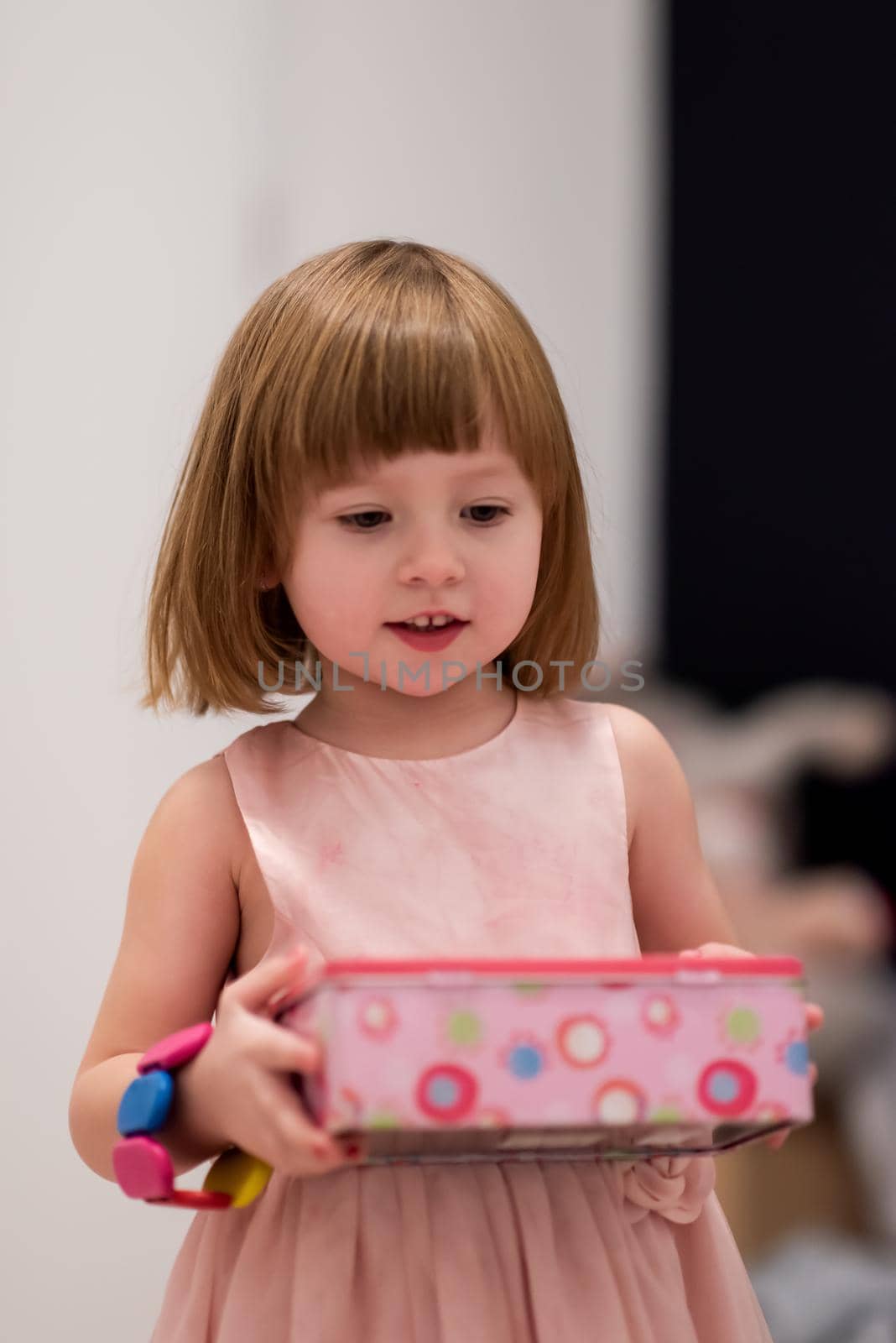 beautiful cute little girl in pink dress enjoying while playing with mother's jewelry from box on the floor at home